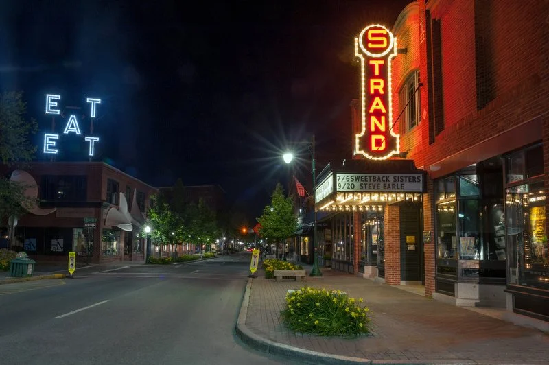 A view of Rockland Main Street illuminated at night with the iconic strand sign, and the legendary eat sign, which was a installation by a famous artist at the Farnsworth Museum