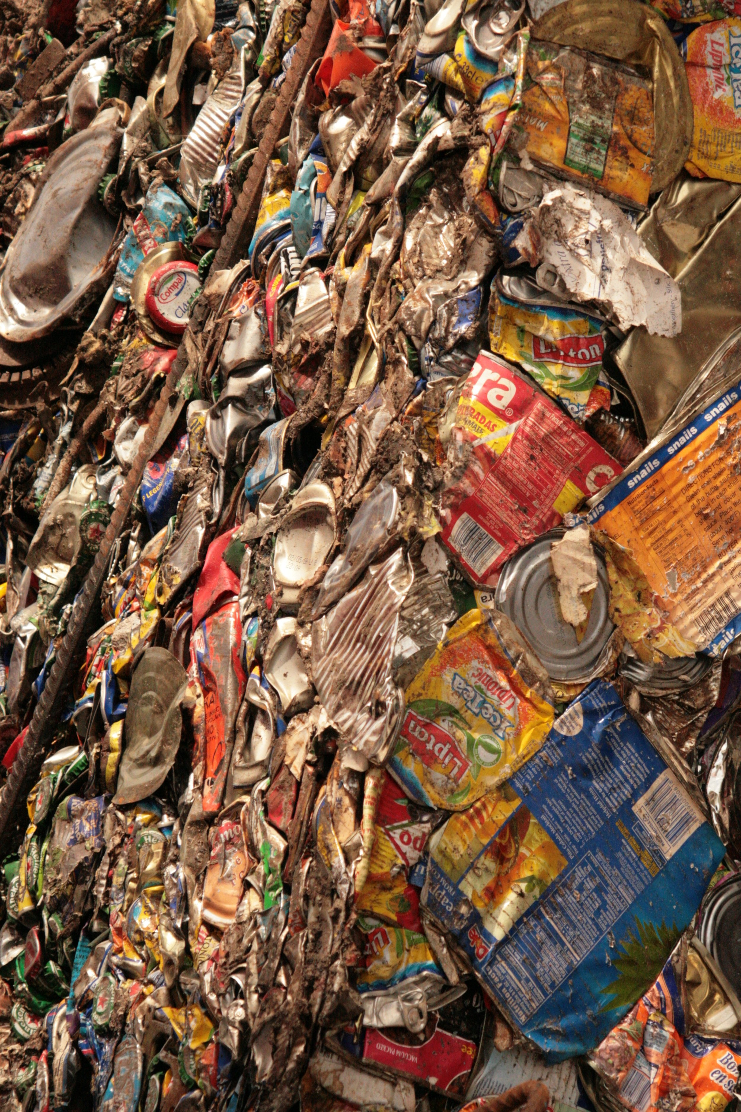 A large stack of crushed and flattened aluminum cans and packaging material, including tins and snack wrappers, in various colors.