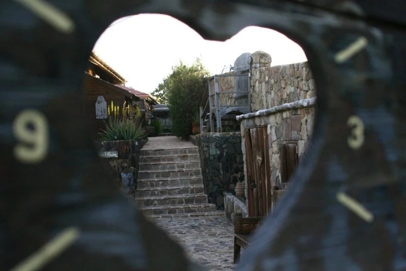 View of stone steps and a stone wall through a circular opening with numbers, resembling the face of a clock, in the foreground.