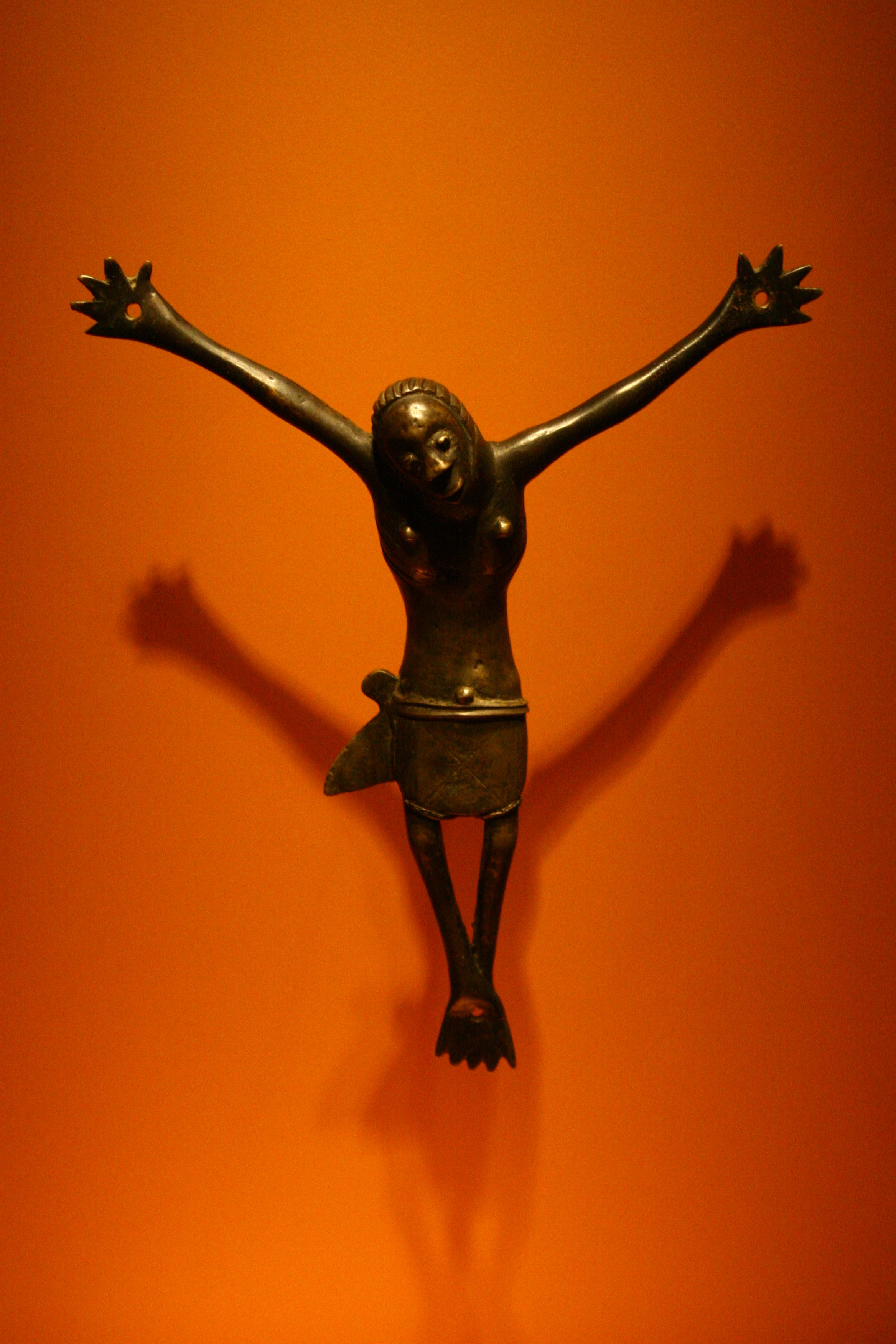Bronze sculpture of a woman with arms raised, casting a shadow on a yellow-orange background.