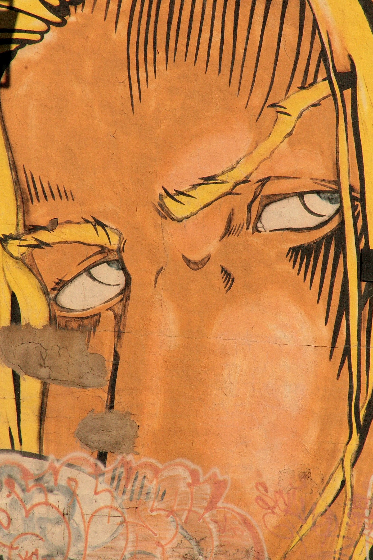 A colorful street art mural depicting a stylized face with one eye closed and the other eye half-open, with exaggerated yellow eyebrows and yellow hair, on an orange background with some graffiti at the bottom.