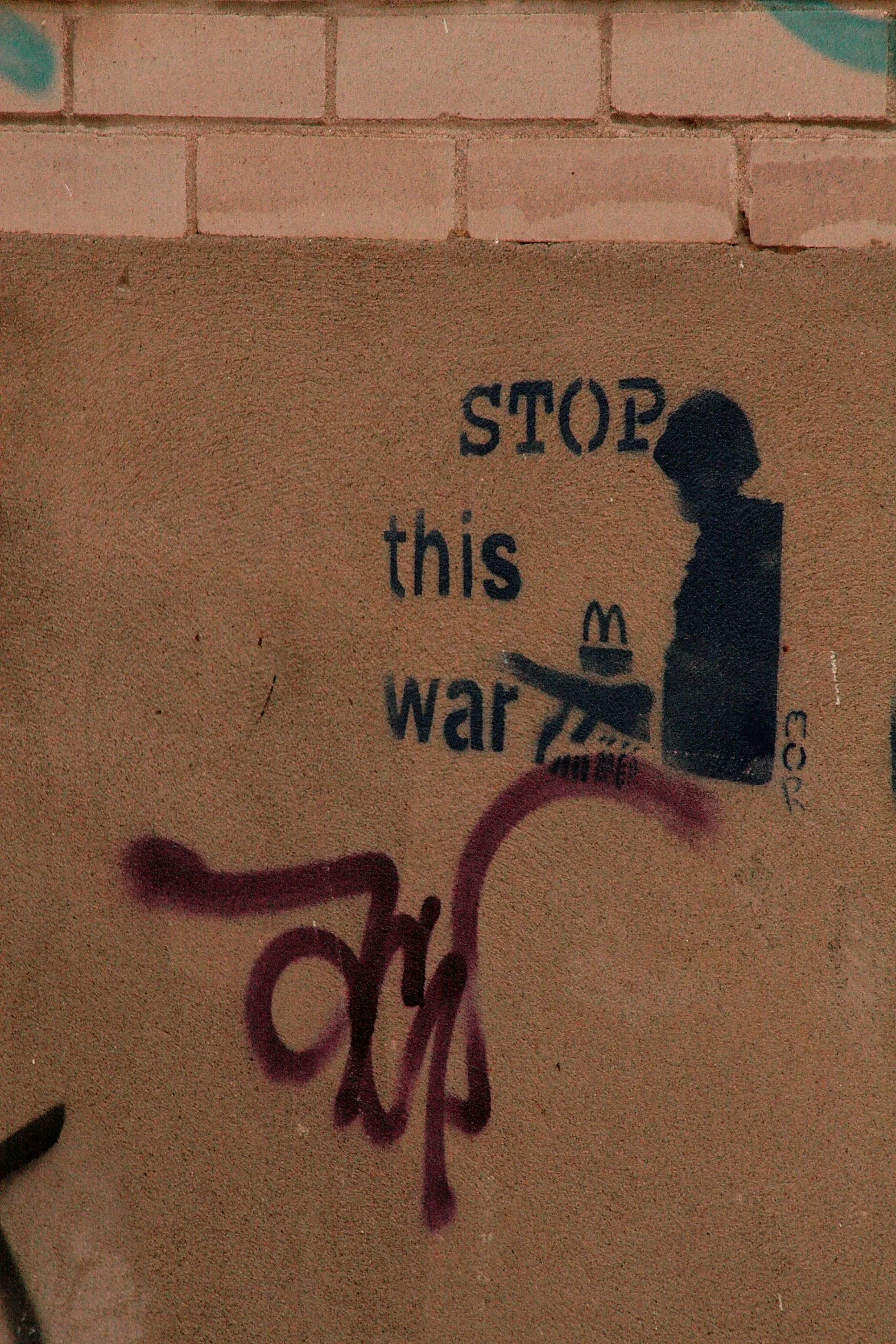 Street art graffiti on a beige wall with the image of a girl in silhouette, along with the text 'STOP this war' and some additional smaller tags.