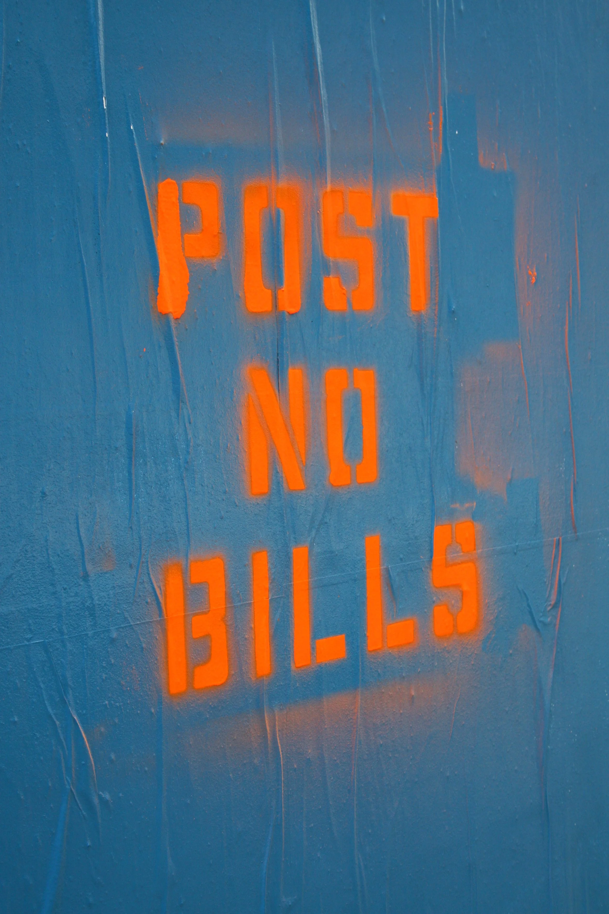 Bright orange neon sign displaying the words 'POST NO BILLS' against a textured blue wall.