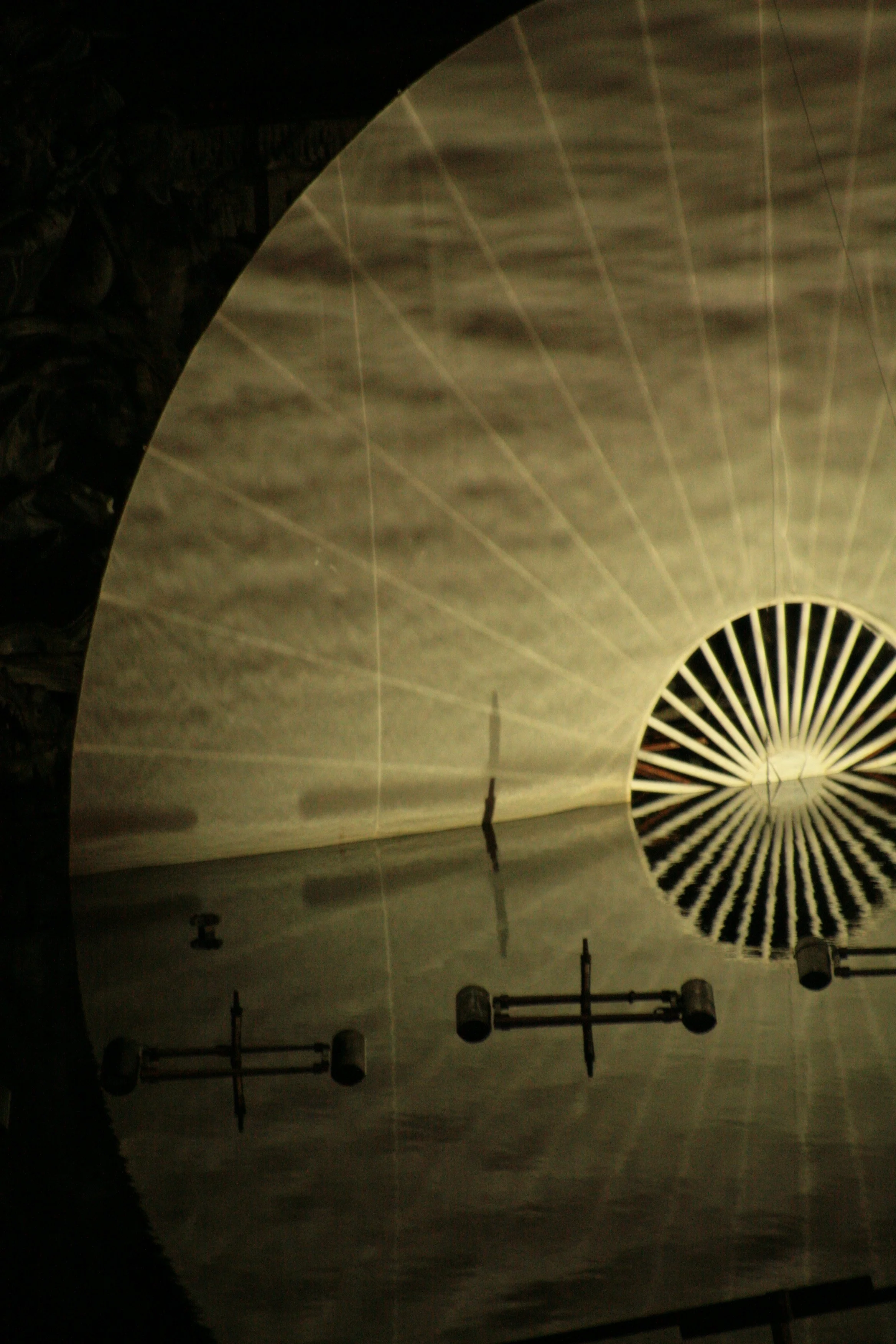 Reflection of a large, circular ceiling light with radiating black and white stripes in a shiny surface, with parts of a wall and small appliances visible.