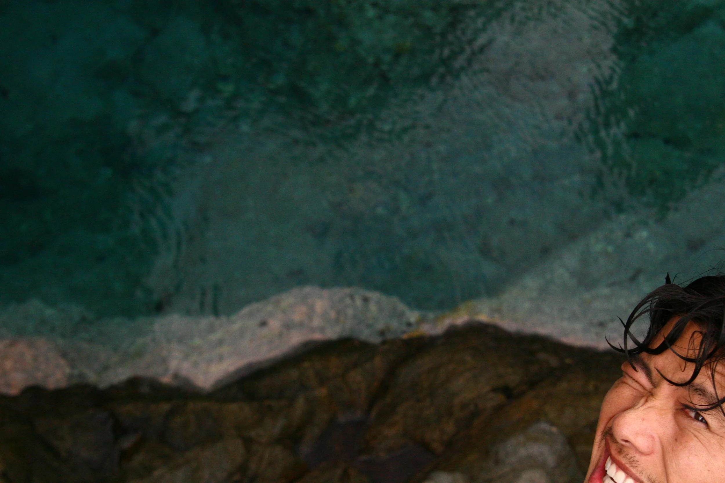 Person with wet hair smiling near rocky water with a greenish surface