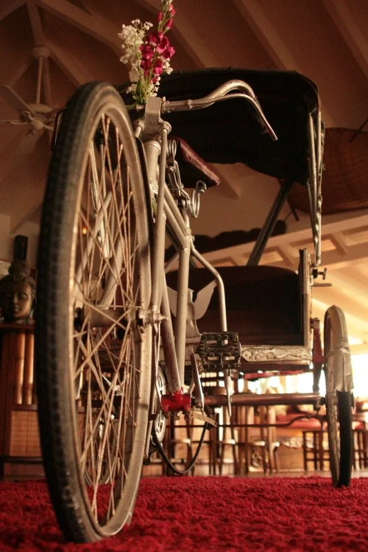 A wheelchair with a flower arrangement on it, inside a room with wooden ceiling and furniture, and a red carpet on the floor.