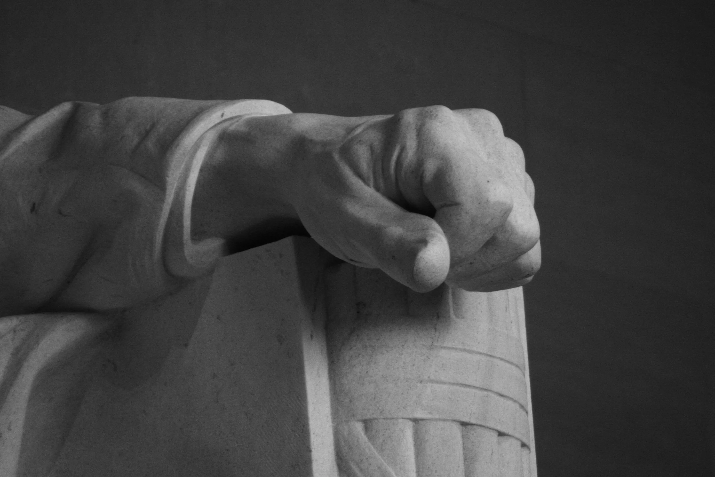 Close-up of the carved stone hand of the Lincoln Memorial sculpture, clenched into a fist, resting on a column.