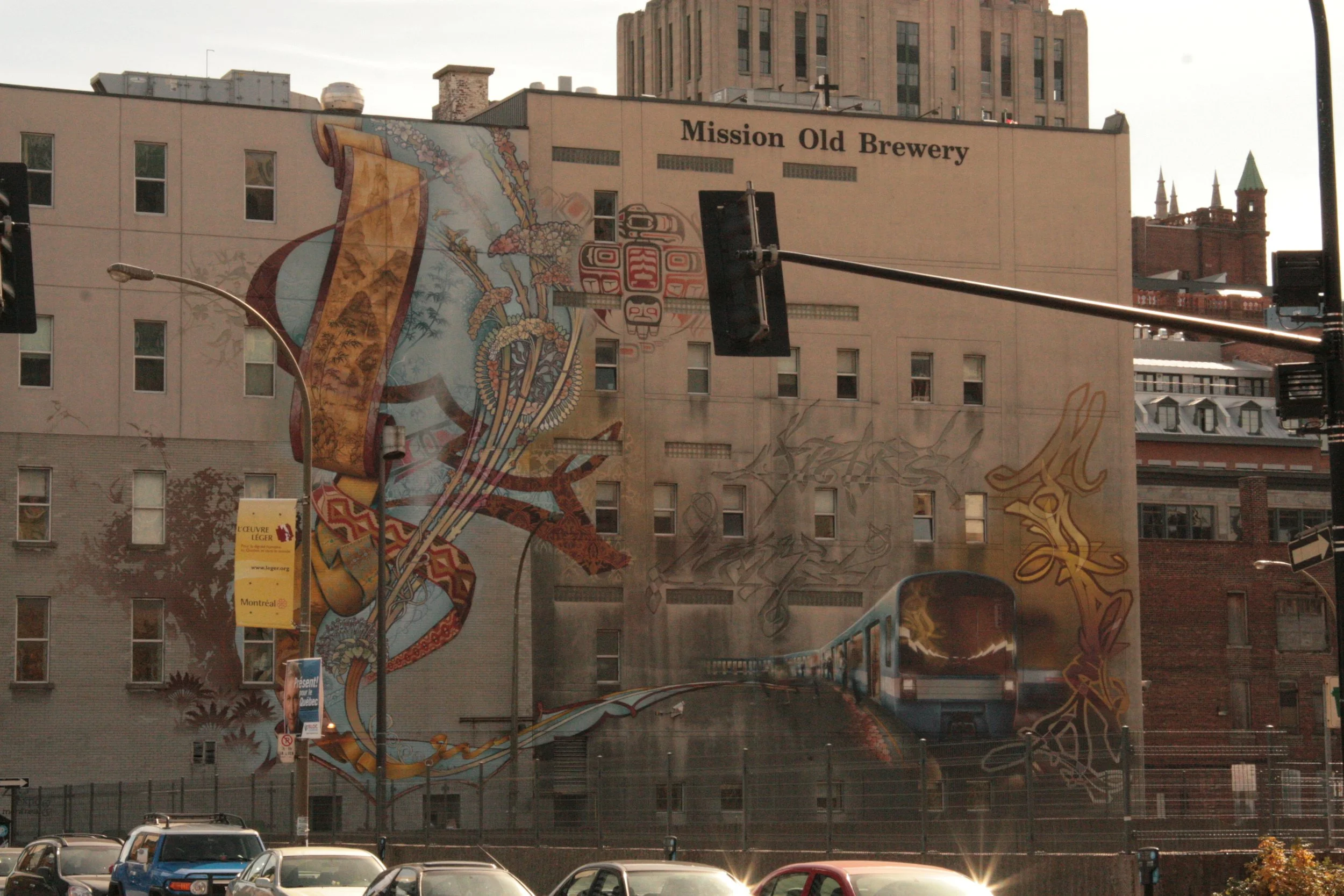 Graffiti mural on a beige building with the text 'Mission Old Brewery,' featuring a colorful outlined train and abstract designs.
