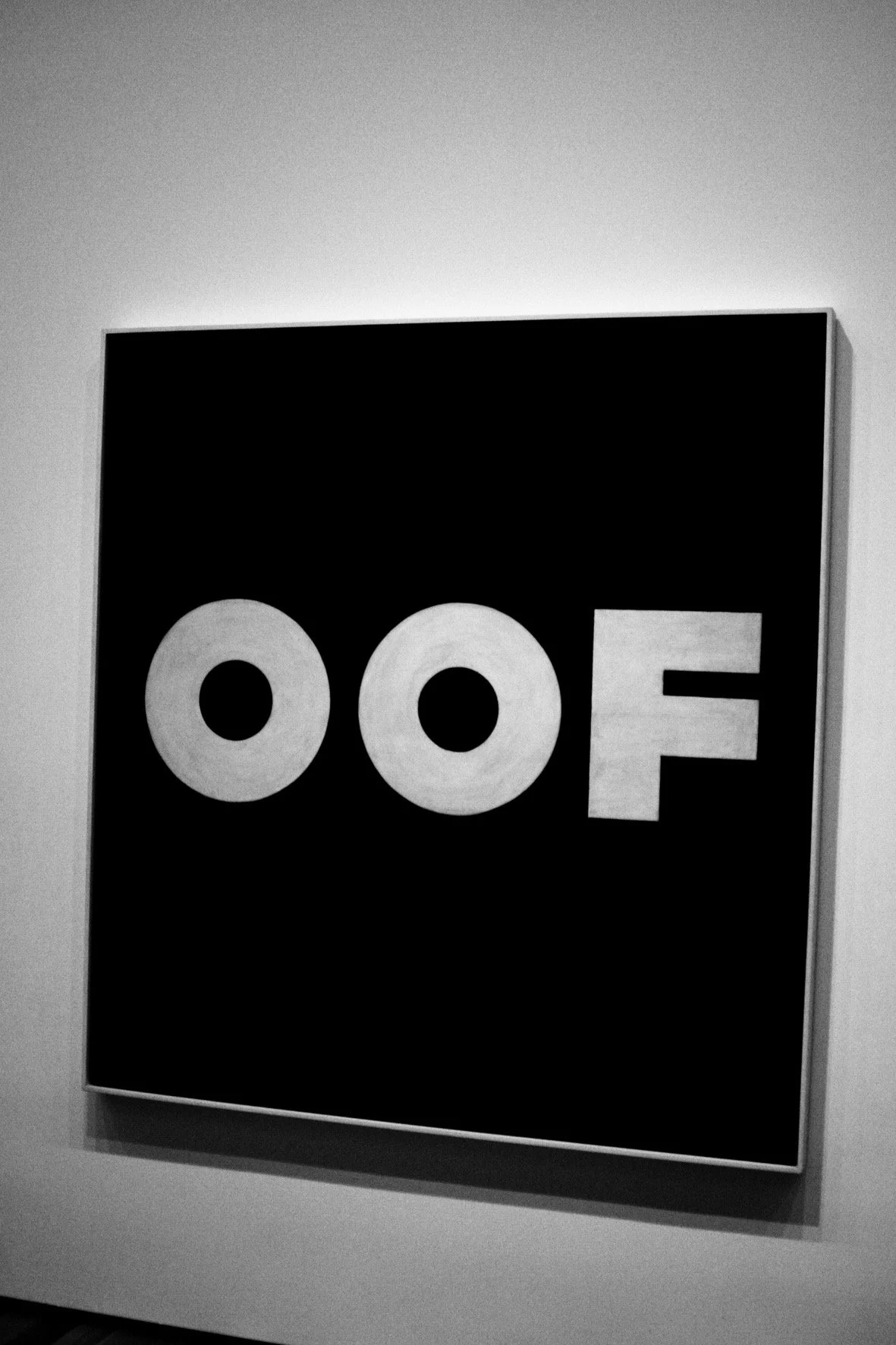 Artwork with the word "OOF" in bold letters on a black background, displayed on a gallery wall.