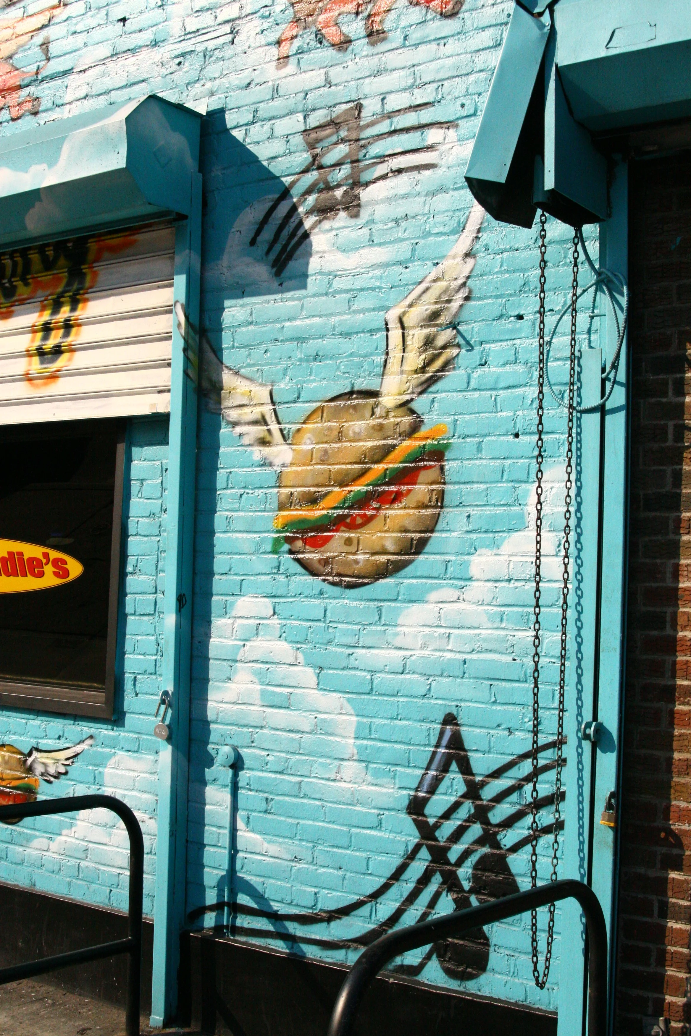 A colorful mural on a brick wall showing a hand holding a hamburger with wings attached, and musical notes painted in the background.