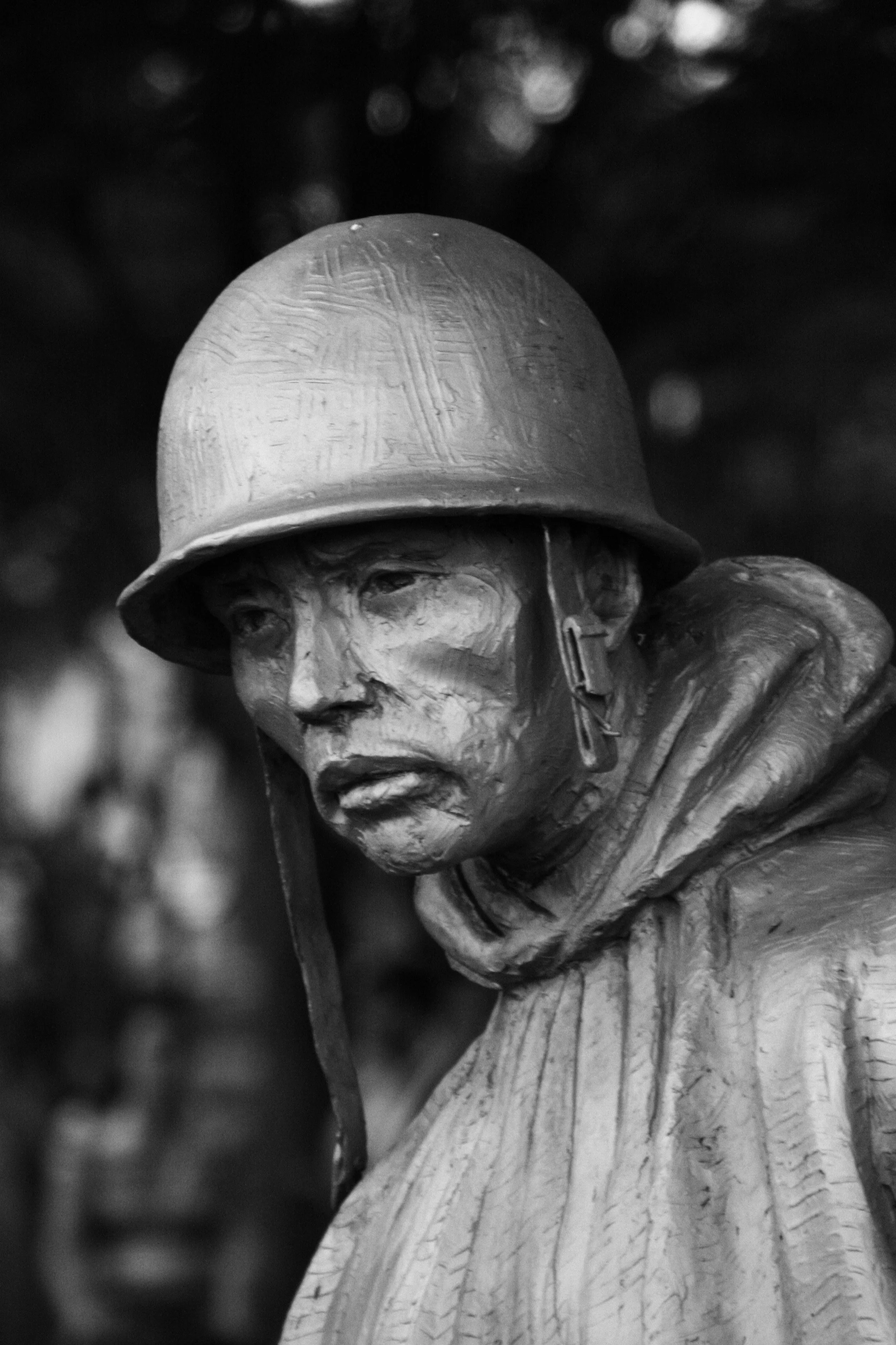 Black and white photograph of a wooden statue of a soldier wearing a helmet and military attire, with a serious expression.