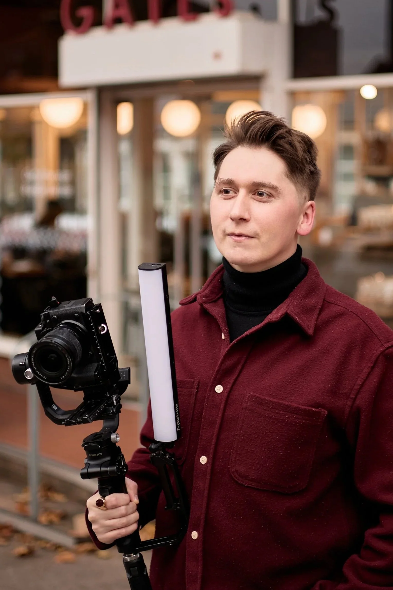 Young man holding a camera stabilizer outside a restaurant with warm lighting.