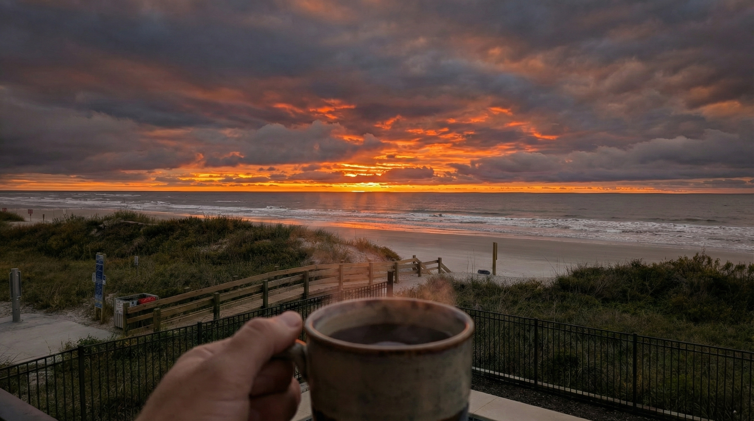 A person holding a cup of coffee while watching the sunrise over the ocean from their balcony in Cherry Grove, North Myrtle Beach.