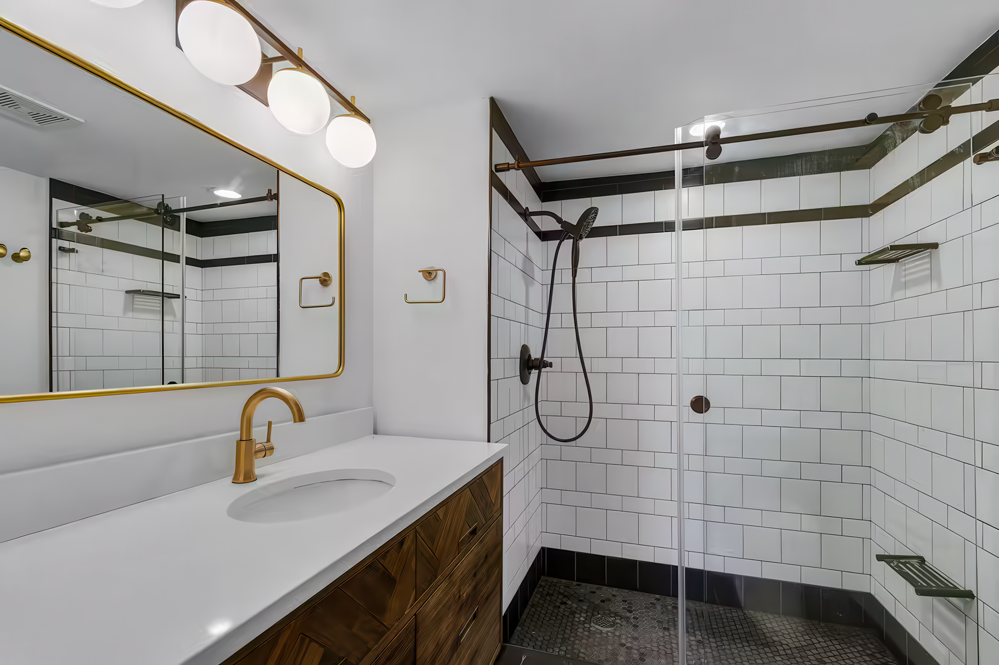 Modern bathroom with white subway tile walls, a gold-framed mirror, white vanity with wooden drawers, and a walk-in shower with black accents and a handheld showerhead.
