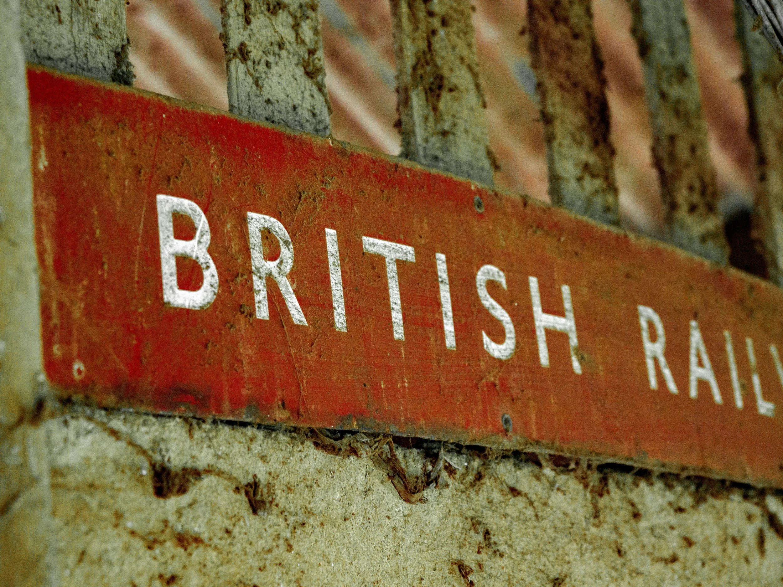 Close-up of an old red metal sign with white text reading 'BRITISH RAIL' attached to a brick wall.