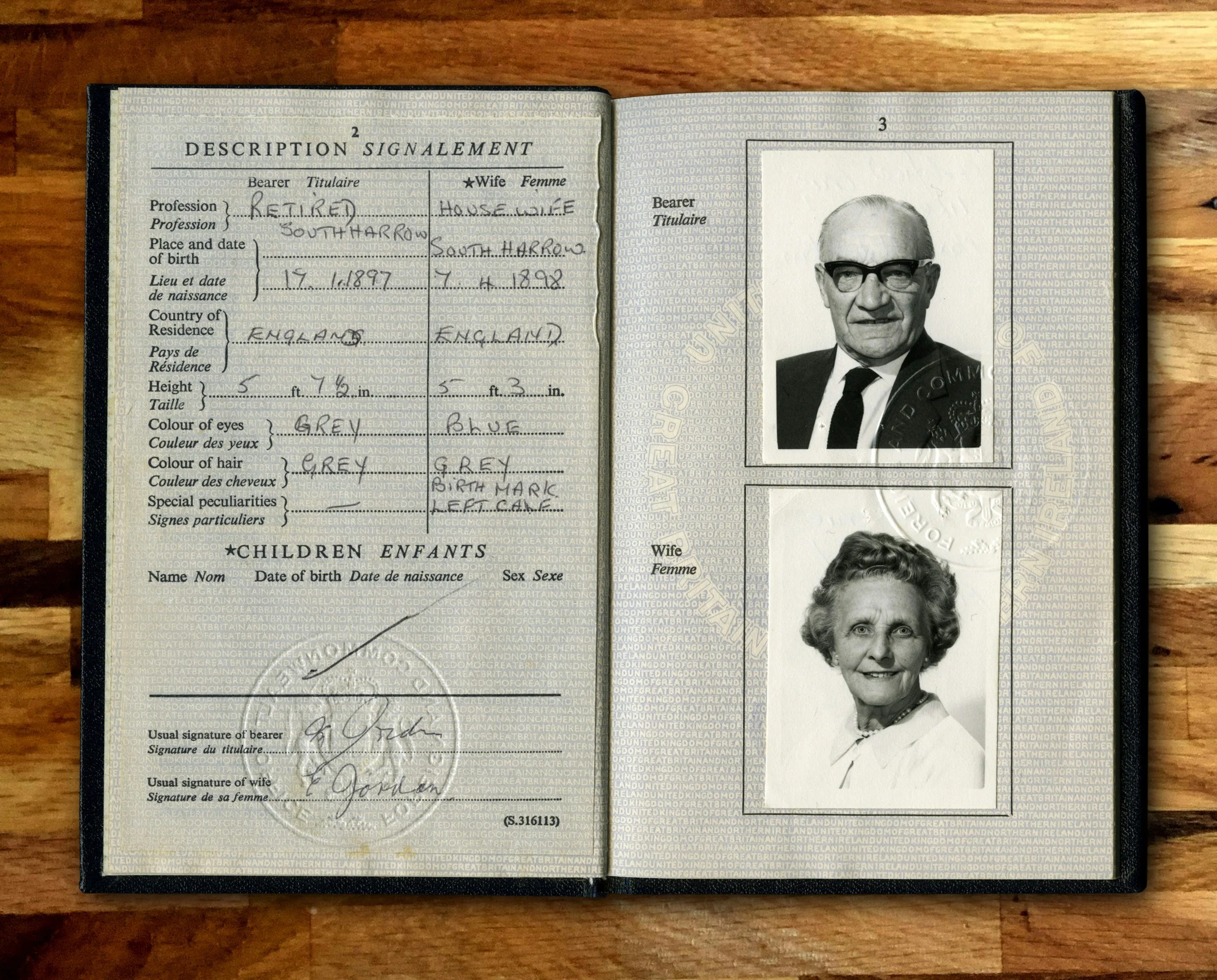Open passport showing personal details and photographs of an elderly man and woman, with the man wearing glasses and a dark suit and the woman smiling, on a wooden surface.