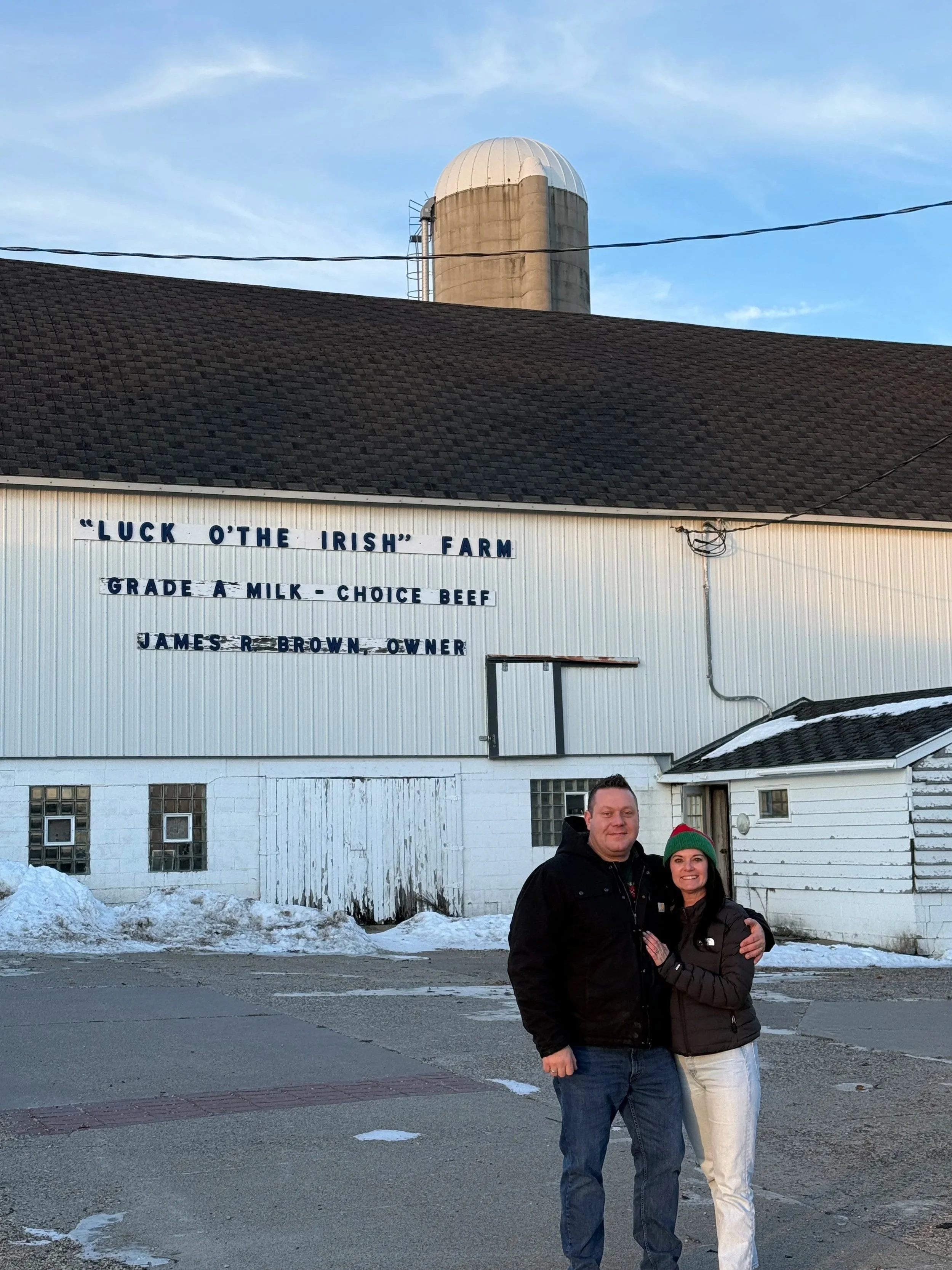 Val and Matt, owners of Luck of the Irish Farm & Distillery, standing in front of their family farm in Roberts, Wisconsin.