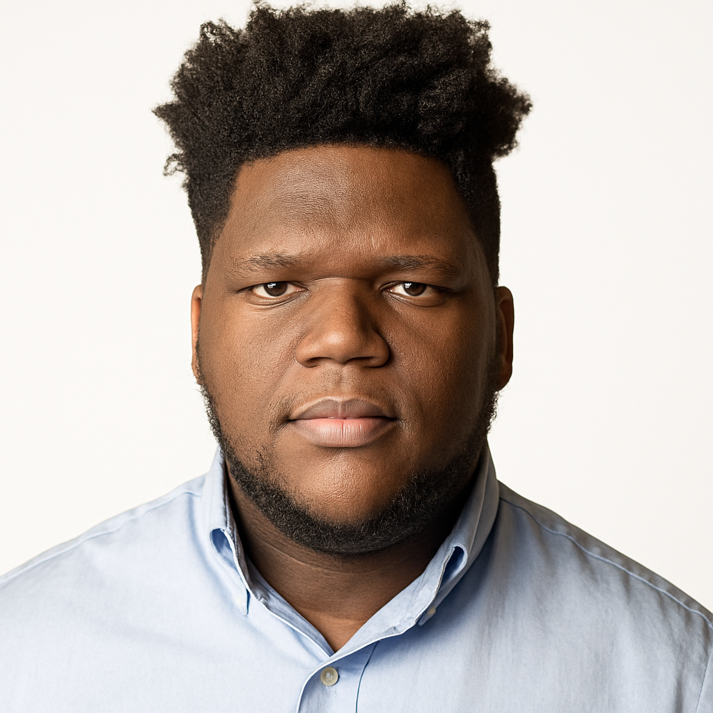 Close-up portrait of a young man with dark skin, thick afro hairstyle, wearing a light blue button-up shirt, against a plain white background.