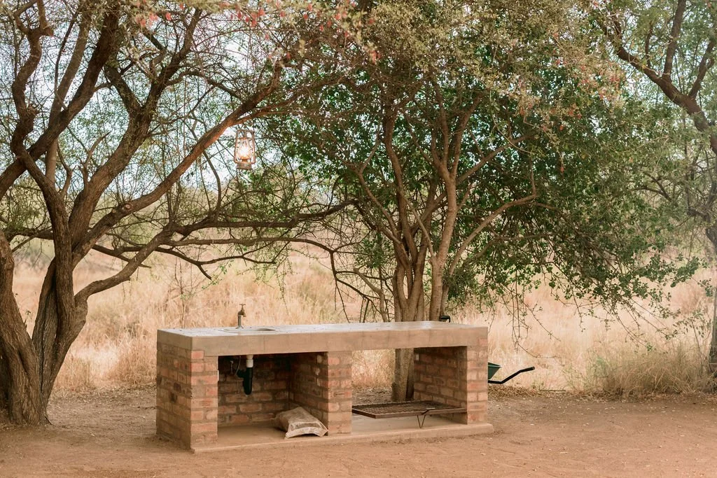Outdoors stone and brick outdoor sink with a faucet under trees, with a lantern hanging from a branch above.