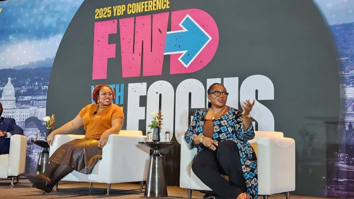 Leanna Baker and Barbara Salami sitting on white chairs on stage at the 2025 YBP Conference, engaging in a discussion. Behind them is a large backdrop with the words "FWD to the Future" and an arrow pointing right, along with a cityscape graphic.