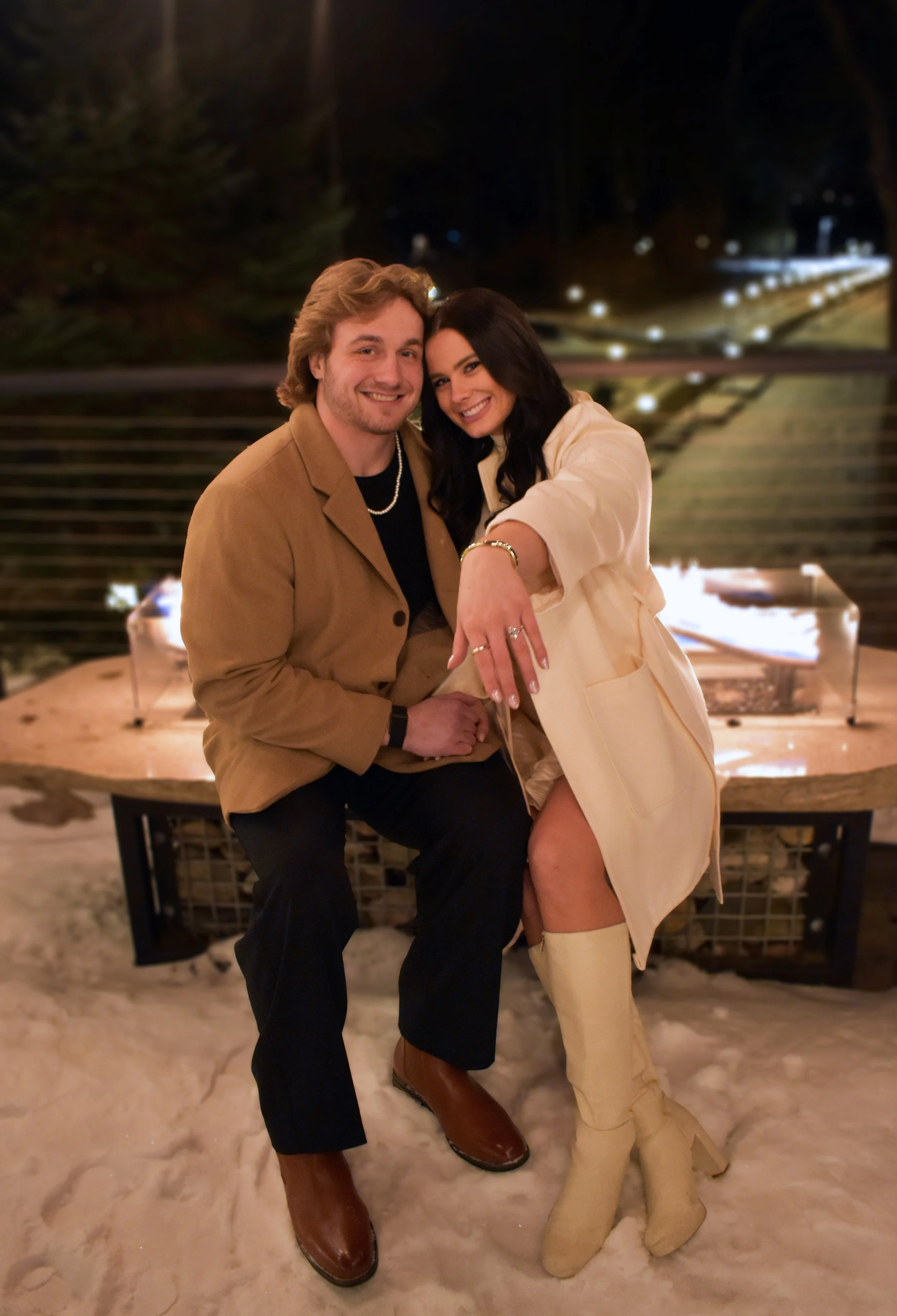 A man and woman sitting together outdoors at night on snow, smiling at the camera.