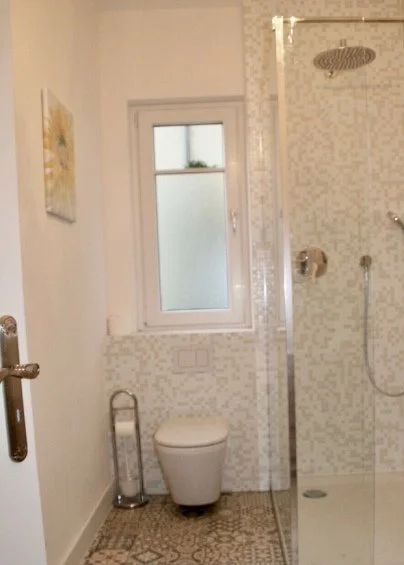 Badezimmer mit WC, Fenster, Dusche, Handtuchhalter und Wanddekoration.