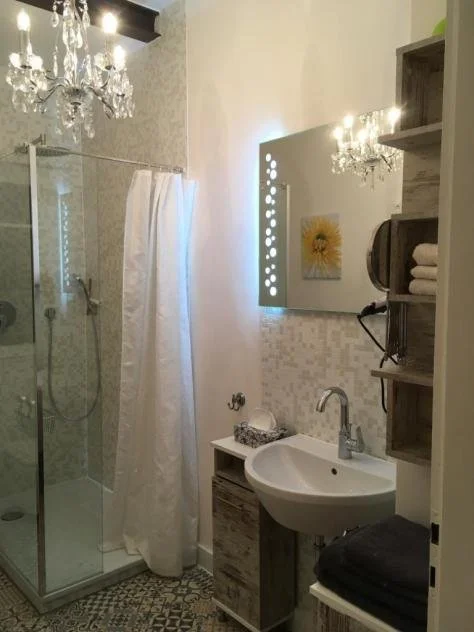 Badezimmer mit Dusche, Waschbecken, Spiegel, Regal mit Handtüchern, Wanddekoration und Kristallleuchter.