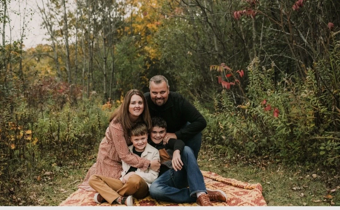 Family of four sitting on a blanket in a forest during fall, smiling at the camera.