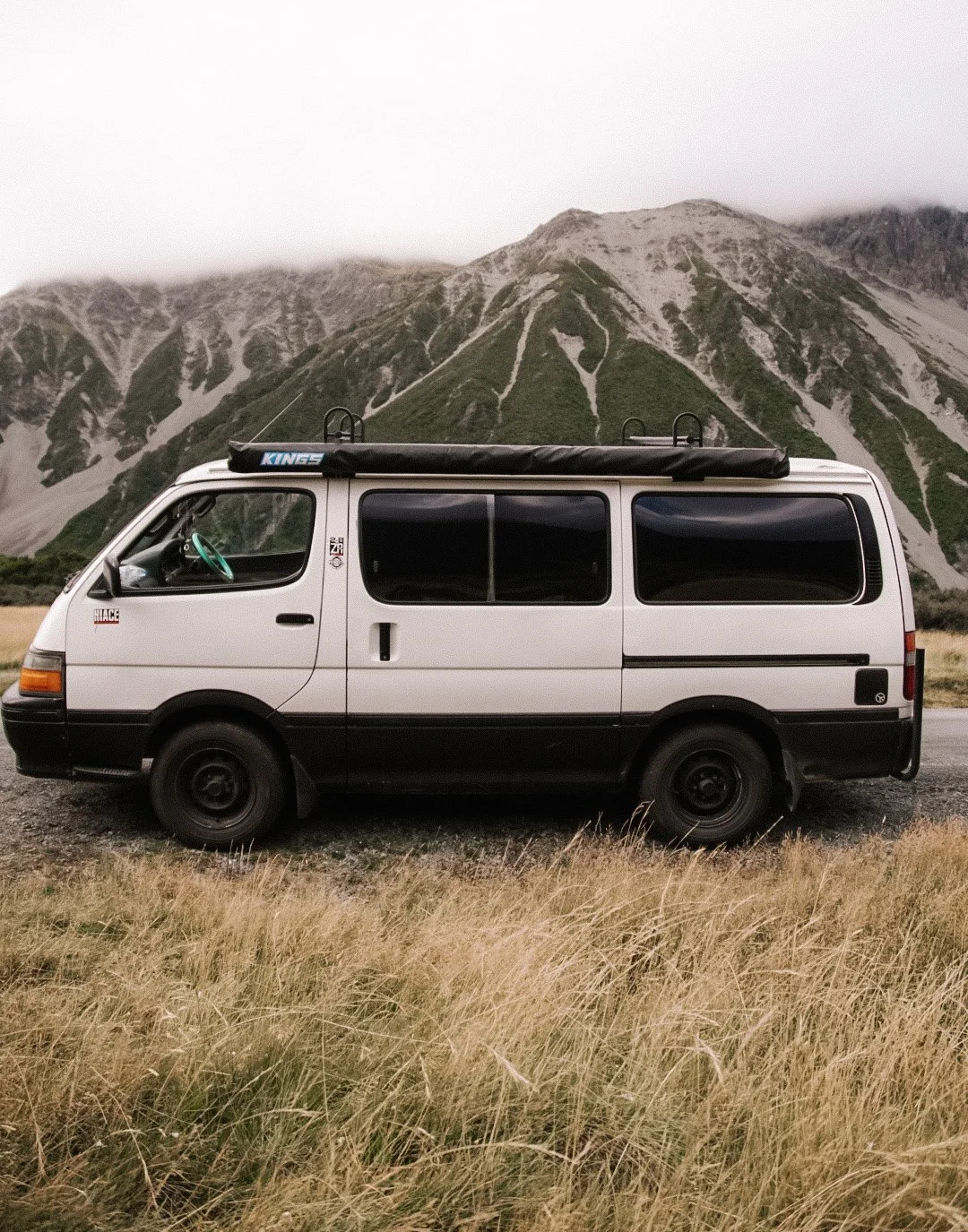 White camper van parked on grassy field with mountains in the background.
