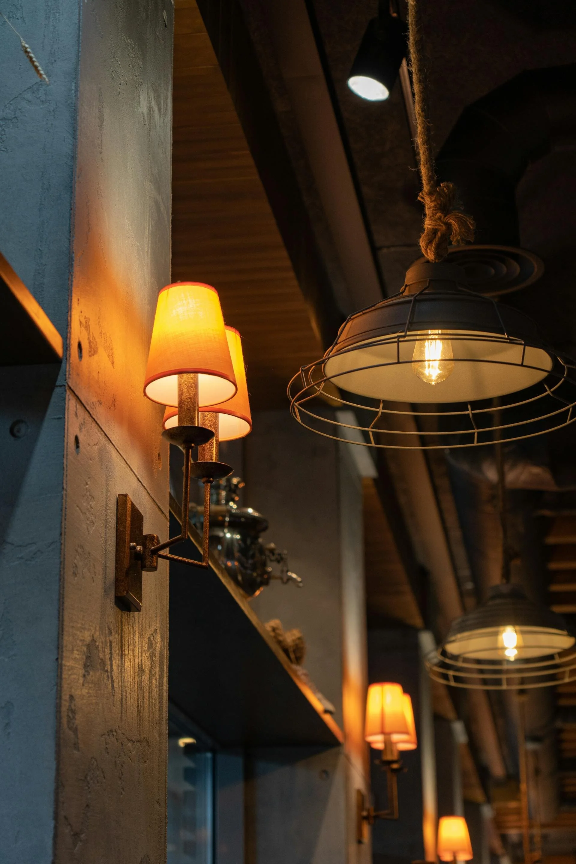 Dimly lit interior with industrial-style hanging lamps and wall sconces, wooden ceiling, and textured wall.