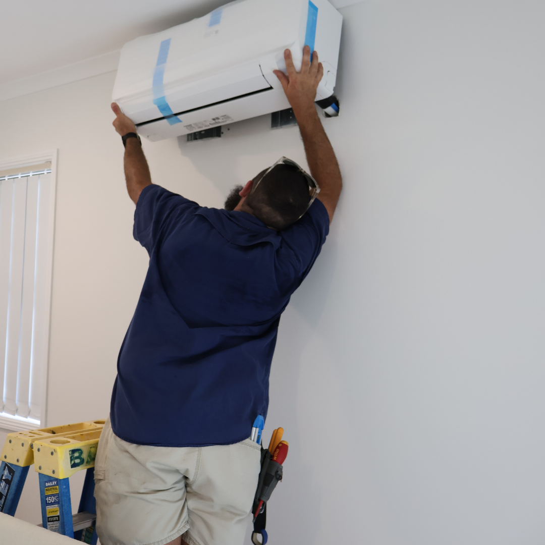 A man installing or adjusting a wall-mounted air conditioning unit on a white wall in a room.