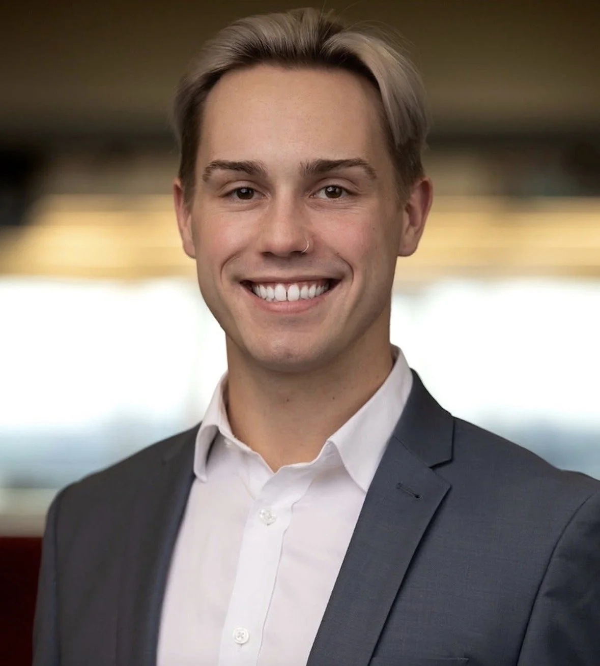 Young man in a suit smiling in an indoor setting with blurred background.