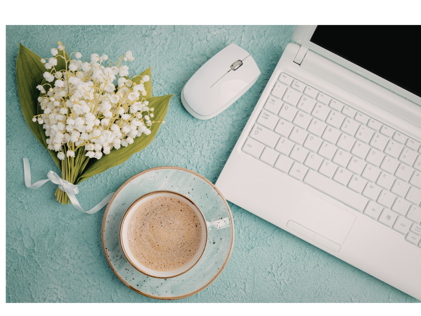 A workspace with a bouquet of white lilies, a cup of coffee on a saucer, a white computer mouse, and a white laptop on a textured teal surface.
