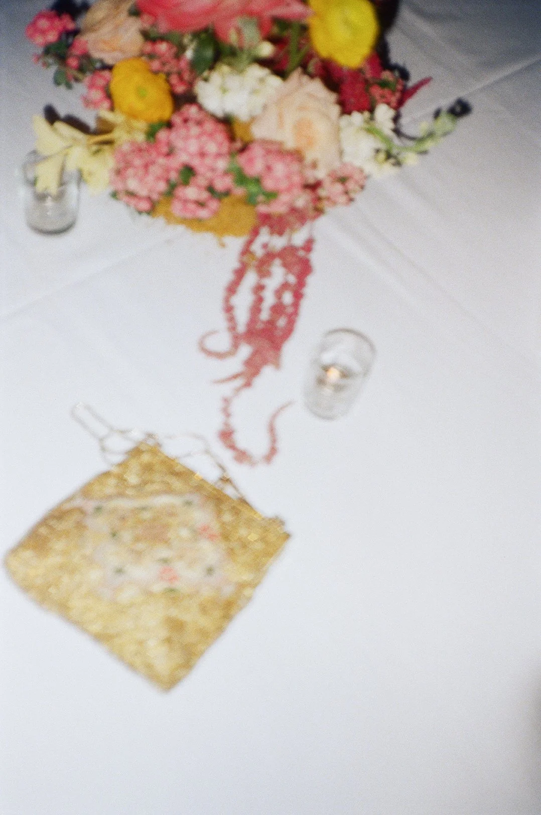 A floral centerpiece with pink, yellow, white, and red flowers on a table with candles and a gold decorative item. Indian Wedding San Francisco in film. 