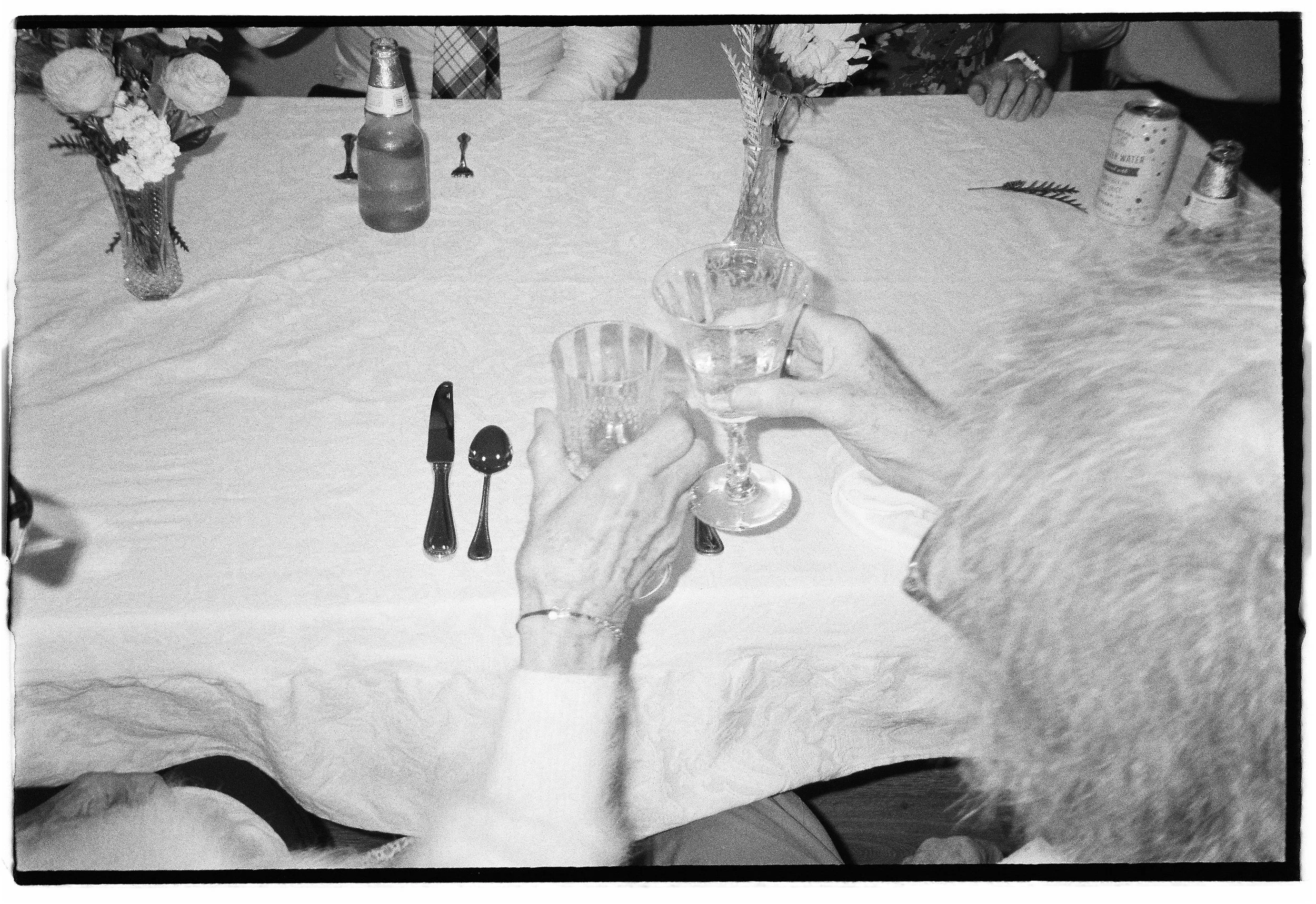 Two elderly women and a man hold wine glasses at a table set with flowers, cutlery, and drinks, celebrating together. Santa Barbara Elopement, grandma toasts in film. 