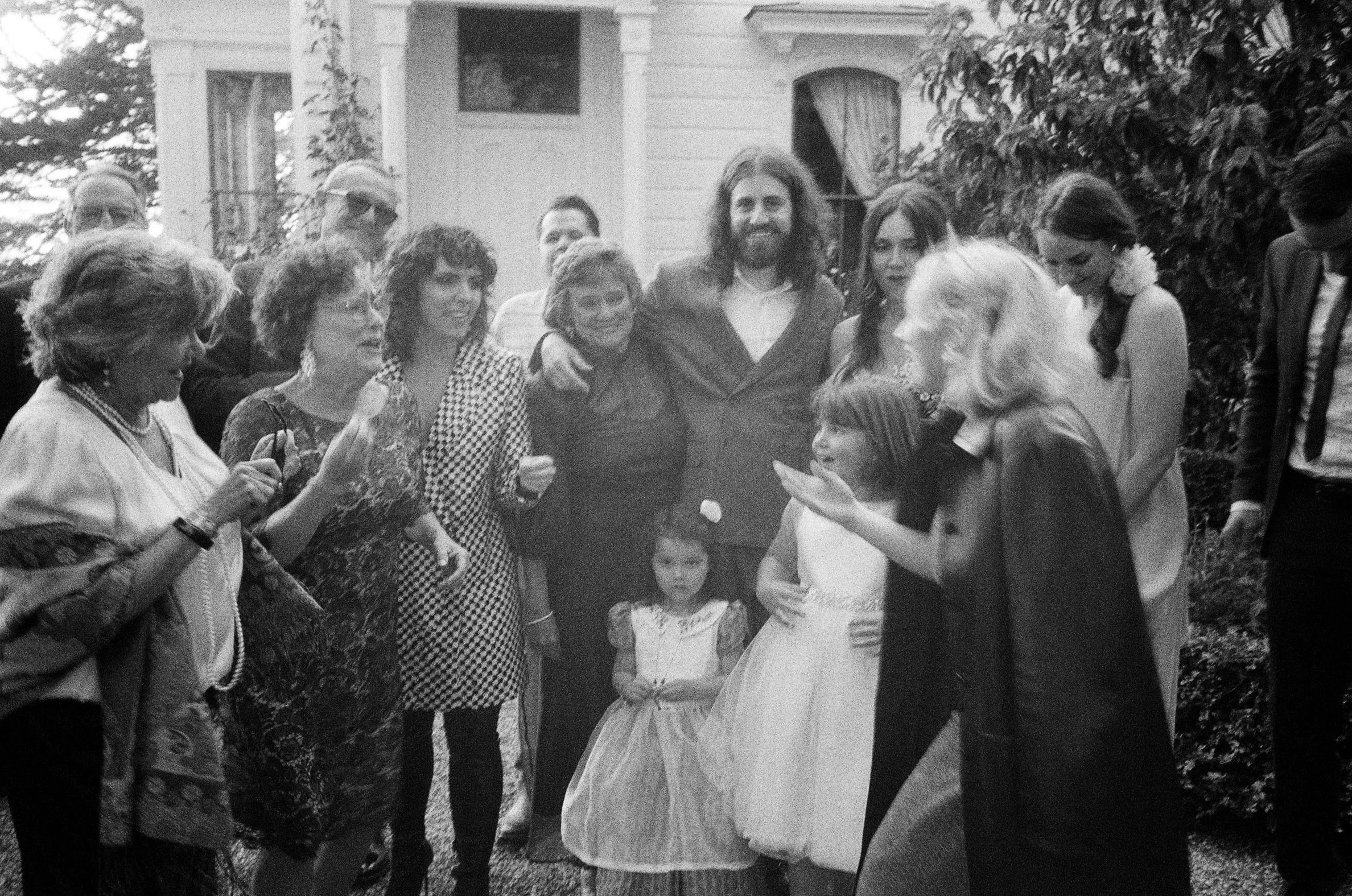 Group of people gathered outside a house, some dressed in formal attire, including women in dresses and children in party dresses, appearing to celebrate or socialize. Switze Farm Westport, California. 