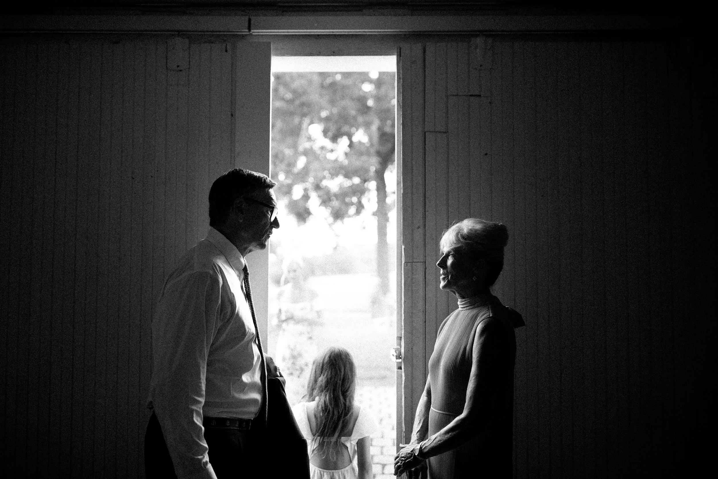 Black and white photo of a man and woman standing inside in front of a door opening to the outdoors. They are facing each other and appear to be engaged in conversation.