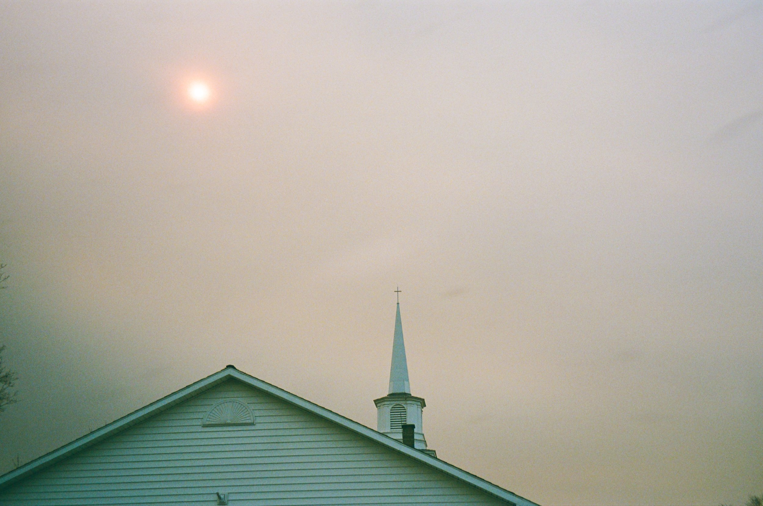 A church with a steeple against a cloudy sky, with the moon faintly visible. Upstate New York, Film. 