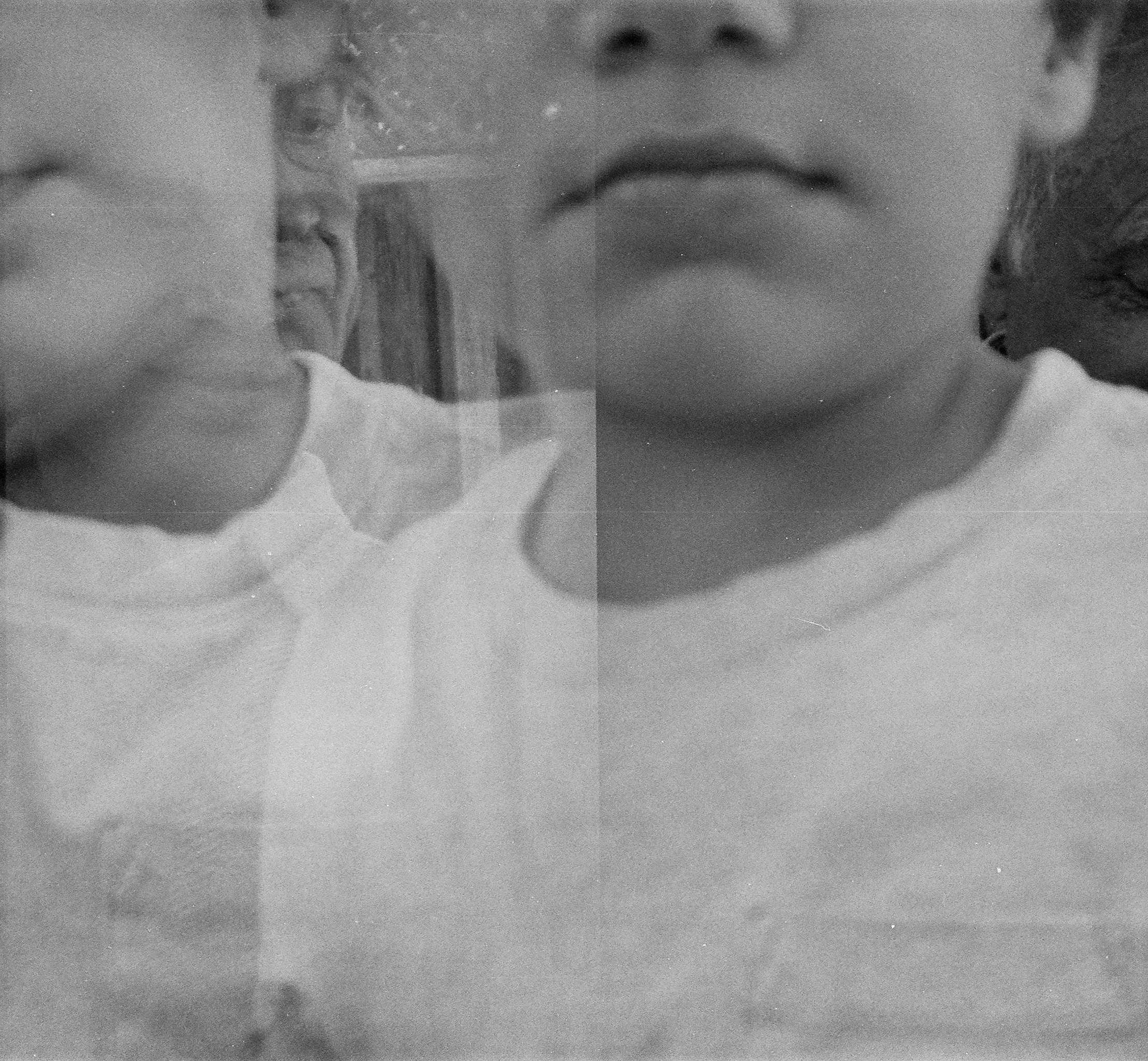 A black and white photo of a child with short curly hair, wearing a white shirt, looking to the side, with a faint reflection of the face visible in the glass behind them.