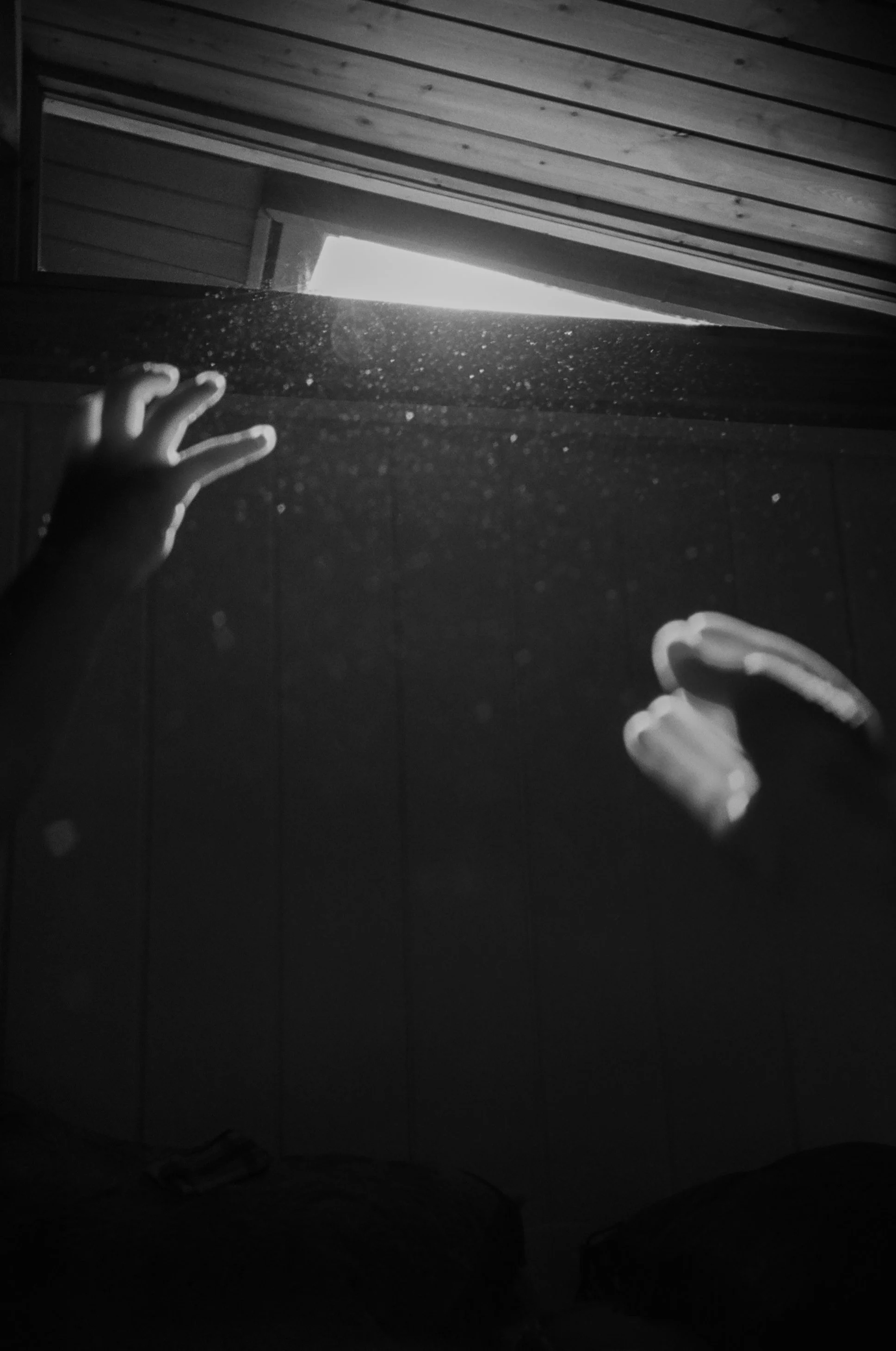 Child with outstretched arms reaching up towards an open attic hatch with sunlight streaming in, black and white photo.