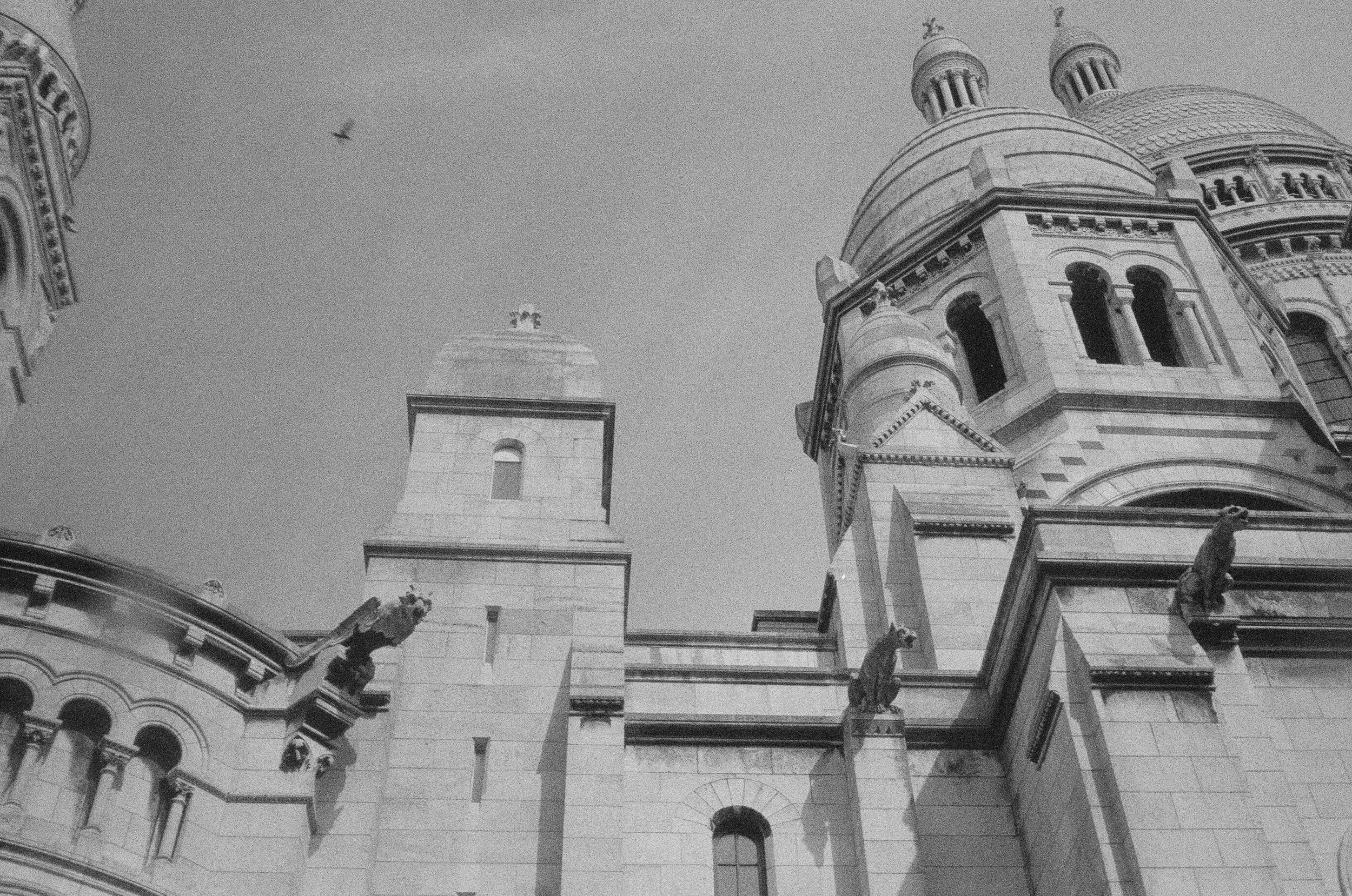 Black and white photo of an ornate, historic building with domes and statues, viewed from below.