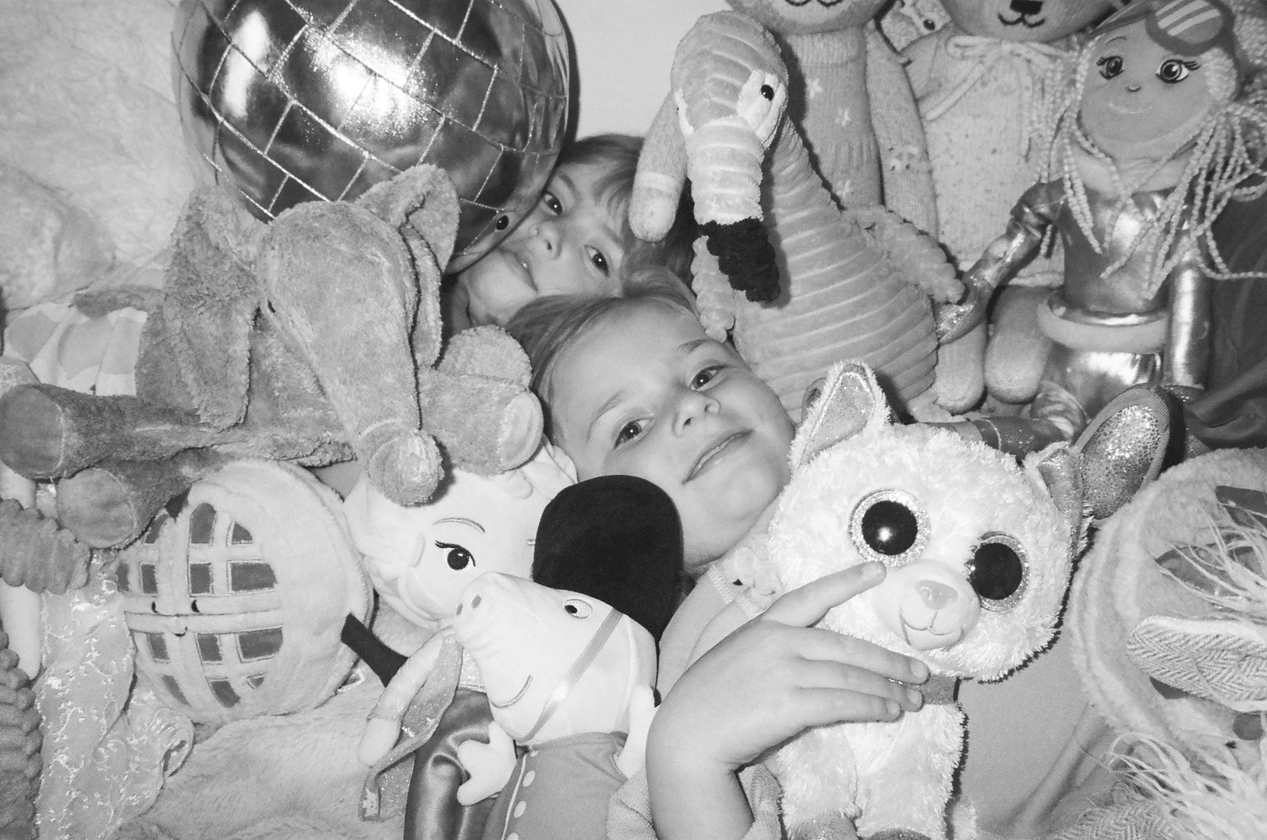 Two young children surrounded by various stuffed animals and toys, smiling and playing. San Francisco family photos in film. 