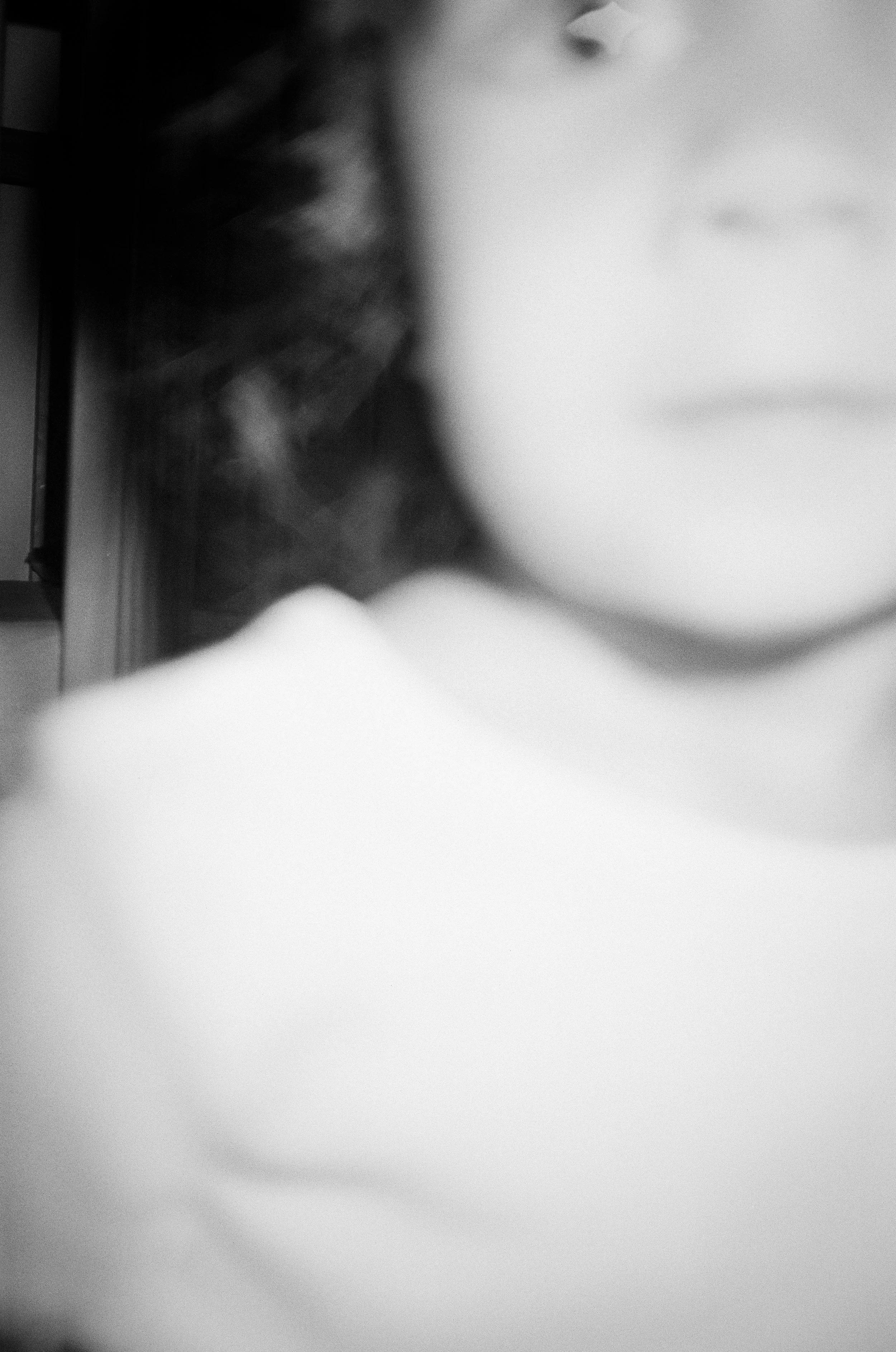 Close-up black and white photo of a person's face, mostly out of focus, with part of their shoulder visible. Oakland family film photos 