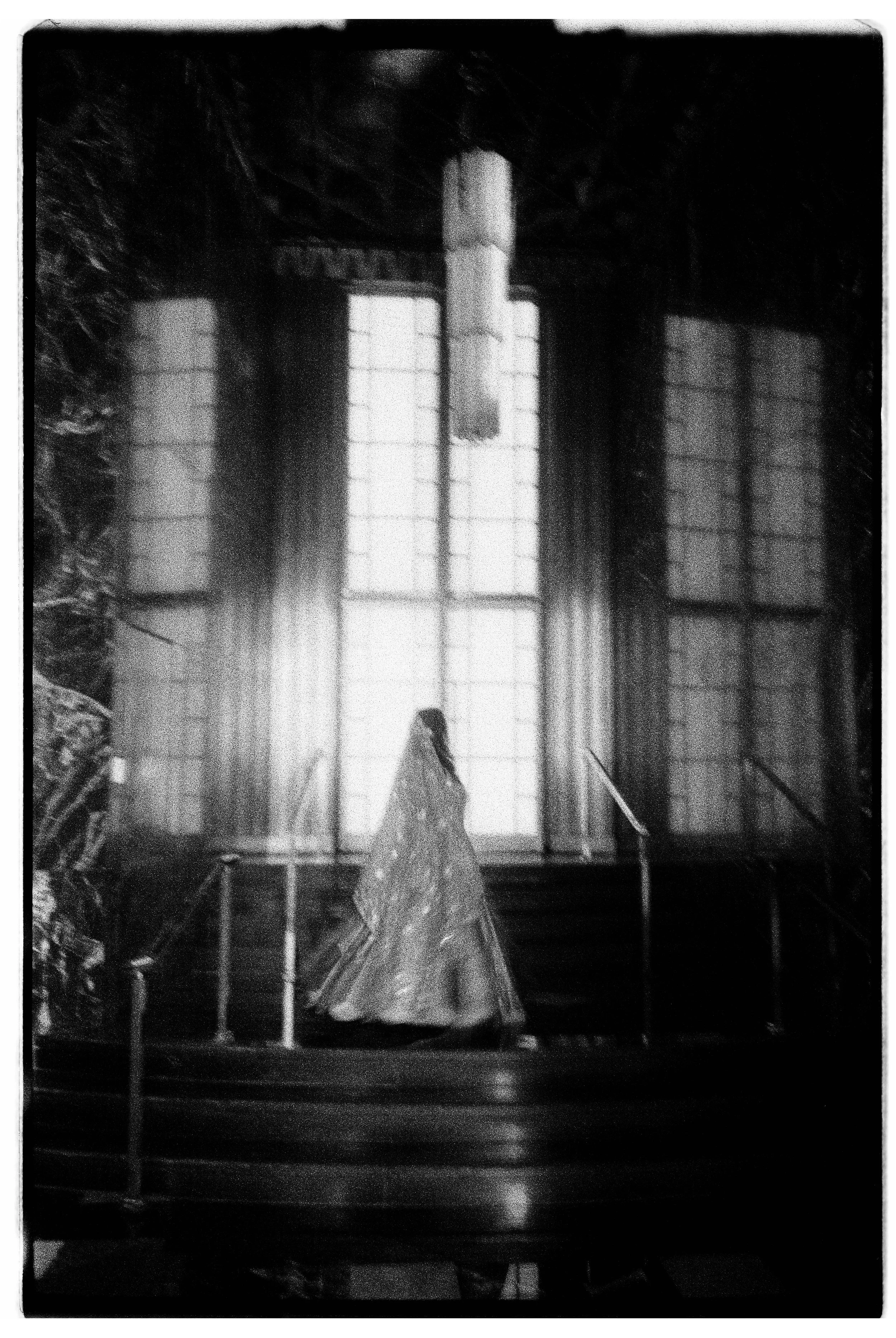 A woman in an elegant, flowing gown walking up a staircase inside a building with large, backlit windows. Indian Wedding San Francisco in film .