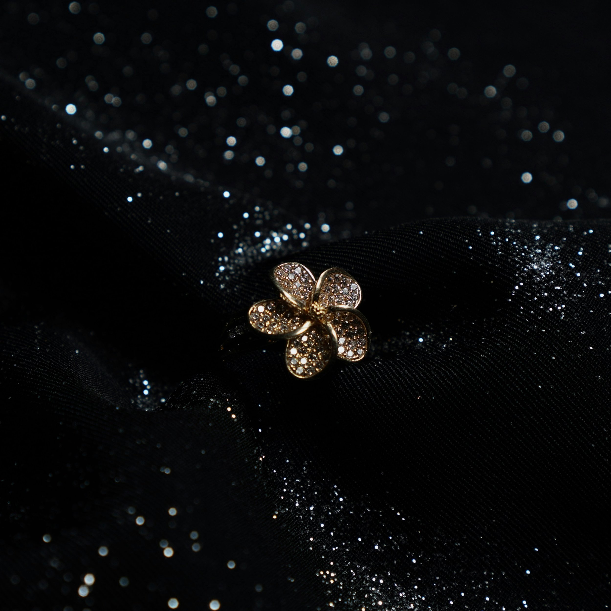 A gold flower-shaped brooch with embedded diamonds on a black, glittery fabric background.