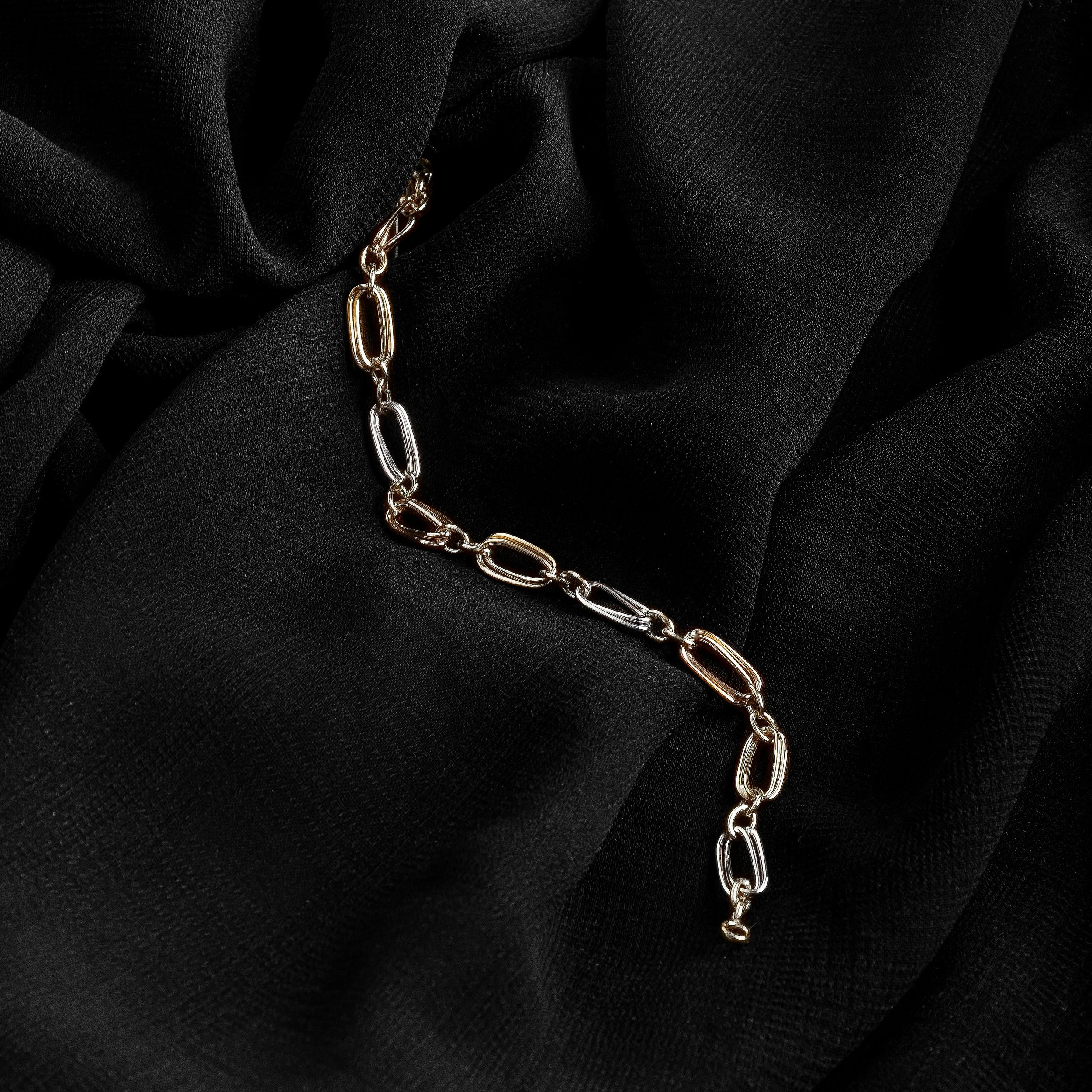 Gold chain bracelet with oval links resting on black satin fabric.