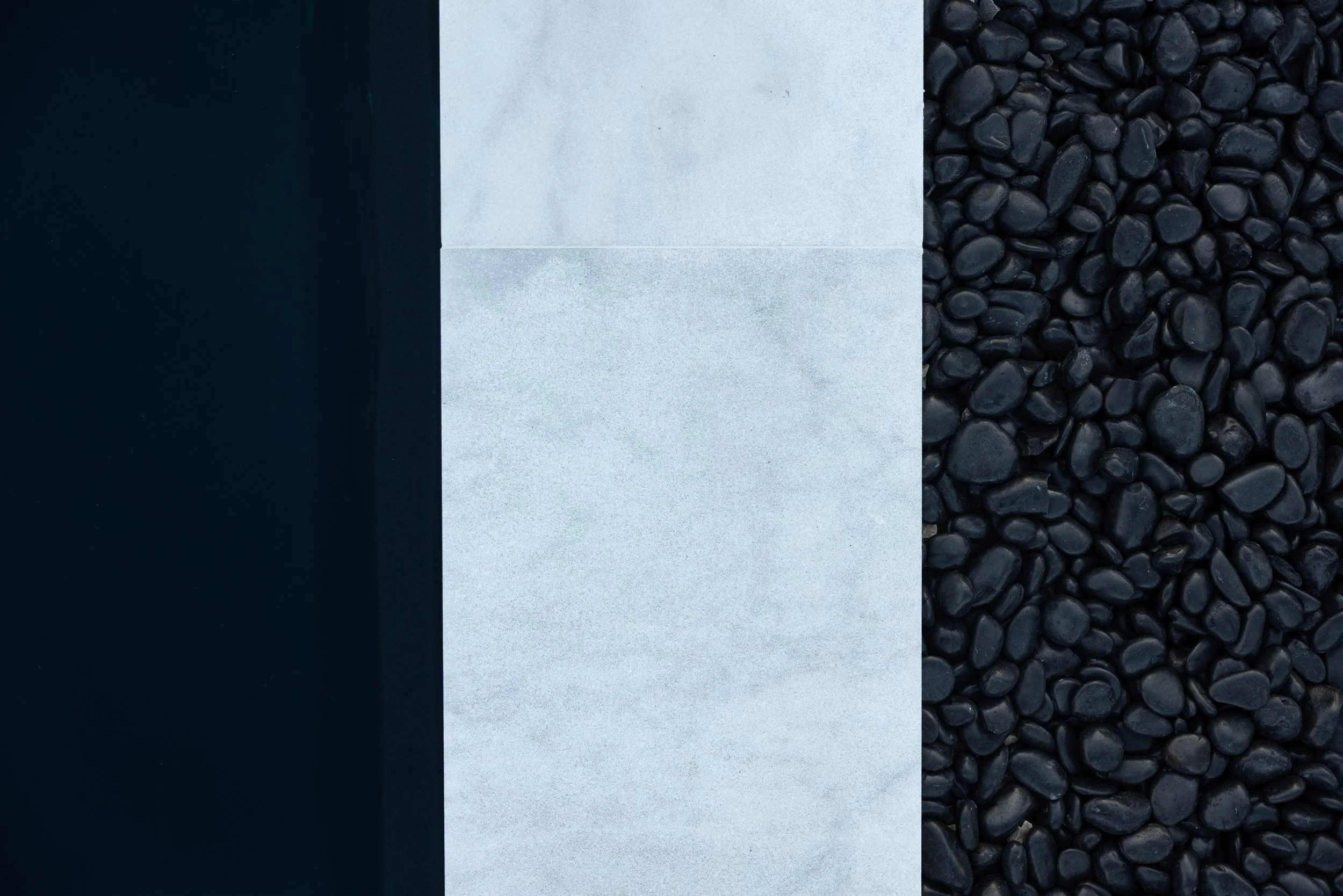 A photograph of three vertical sections: black material on the left, light gray surface in the middle, and black pebbles on the right.