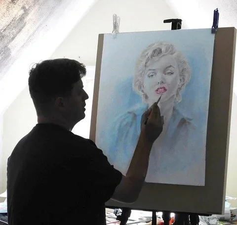 Artist painting a portrait of Marilyn Monroe on an easel.