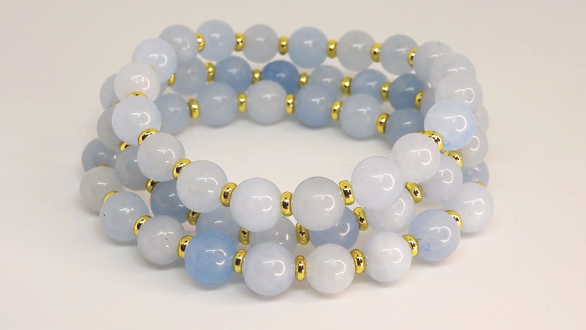 Two beaded bracelets made of light blue and white round beads, with small gold spacers, arranged on a plain white background.