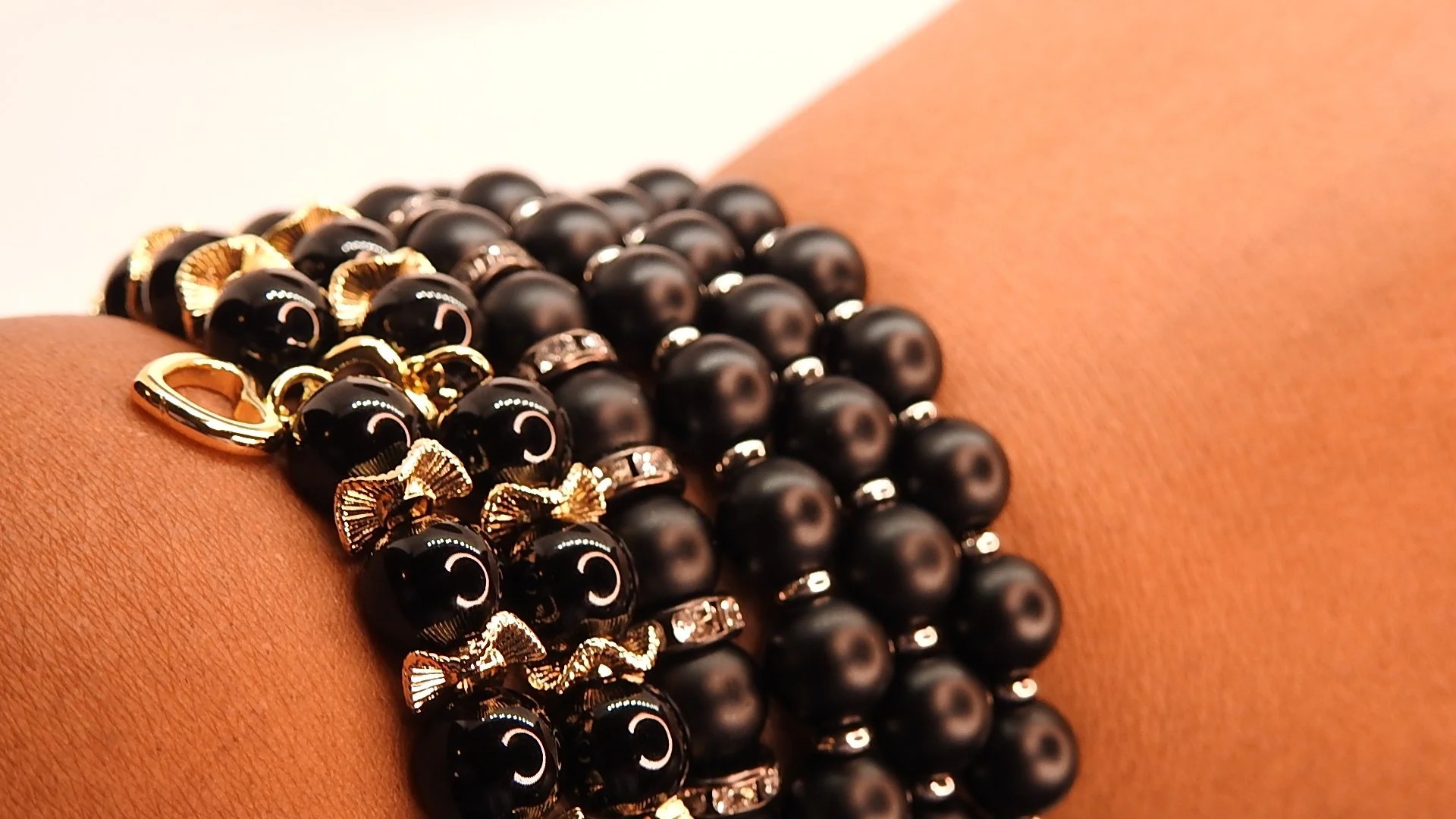 Close-up of a person's wrist adorned with multiple black pearl and gold bead bracelets.